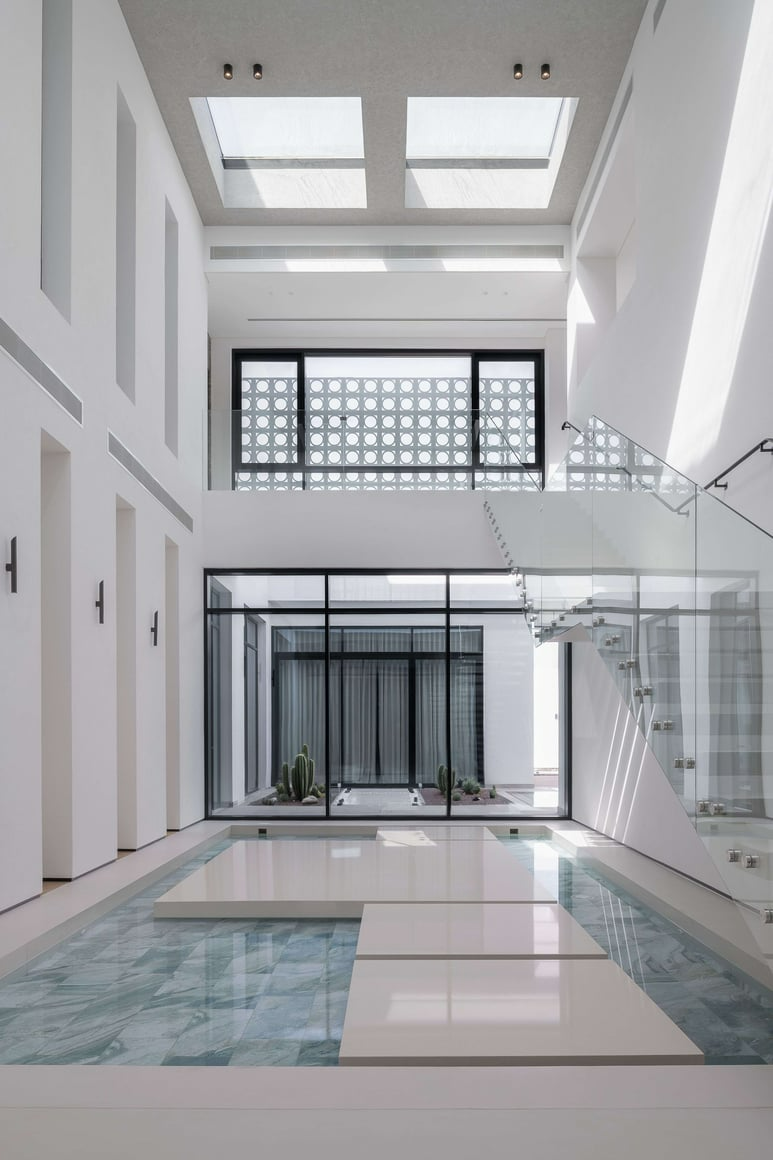 Veil House by ENCLAVE Architects. Photography by Hassen Arante. Double height interior space with white walls, glass staircase, white pavers over pool and windows overlooking courtyard garden.