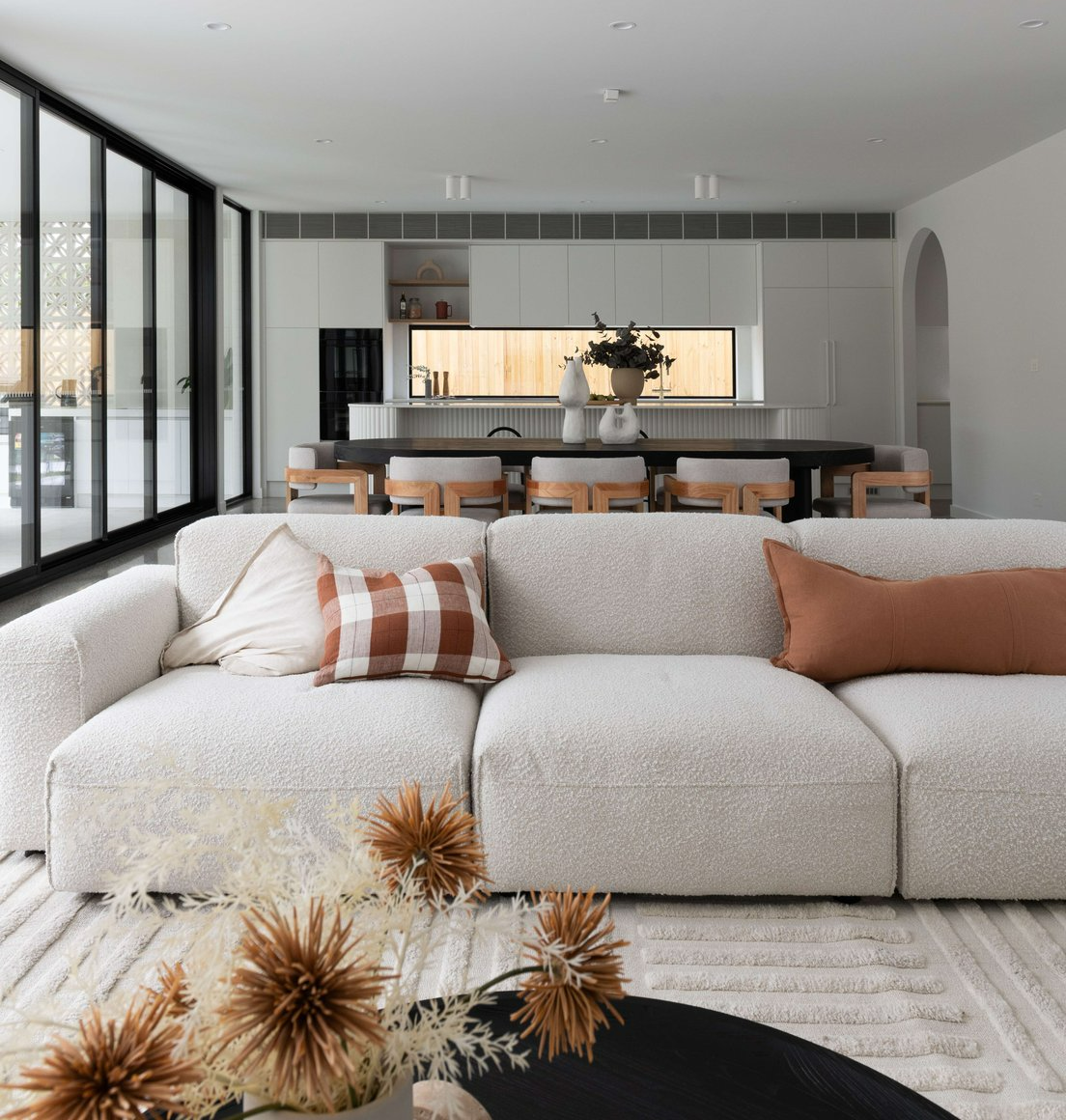 East Keilor One by Eastwood Designers. Photography by Tanya Macheda. Open plan living, dining and kitchen with white boucle couch in foreground and kitchen with white cabinetry in background.