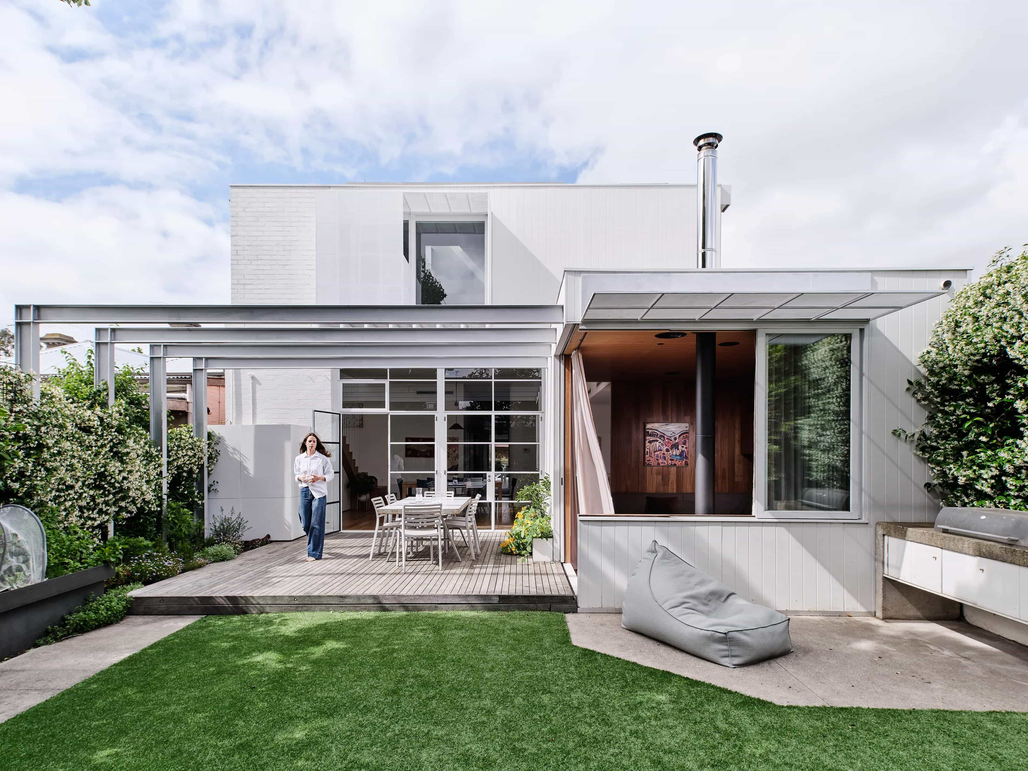 Fitzroy North Residence by True Story. Photography by Dean Bradley. Rear facade of white timber clad home with steel patio and timber decking.