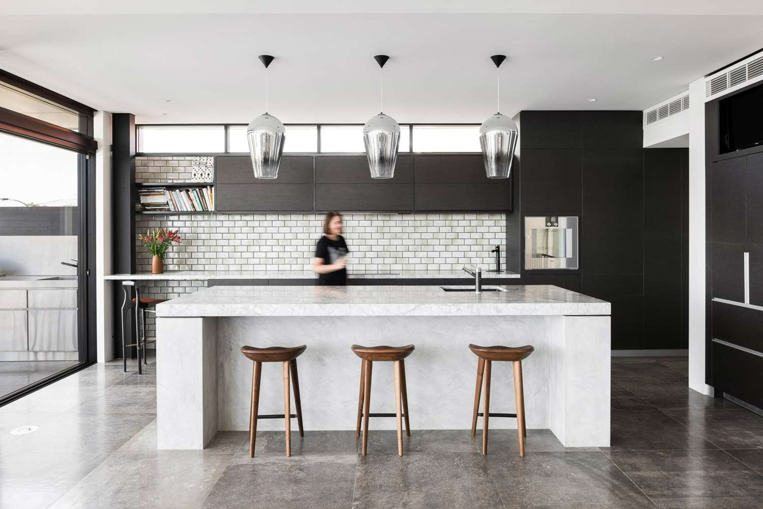 Chauncy Street by Keen Architecture. Phtography by Dion Robeson. Kitchen with white stone island bench, dark grey tiled floors, green subway tile splashback and black cabinets.