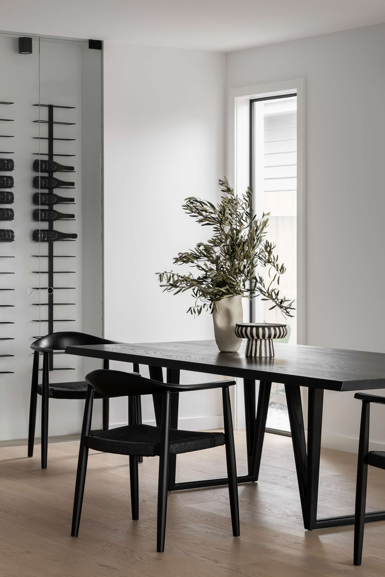 Anderson by Mancini Made. Photography by Timothy Kaye. Dining space with timber flooring, black timber dining table, glass wine wall in background and white walls.