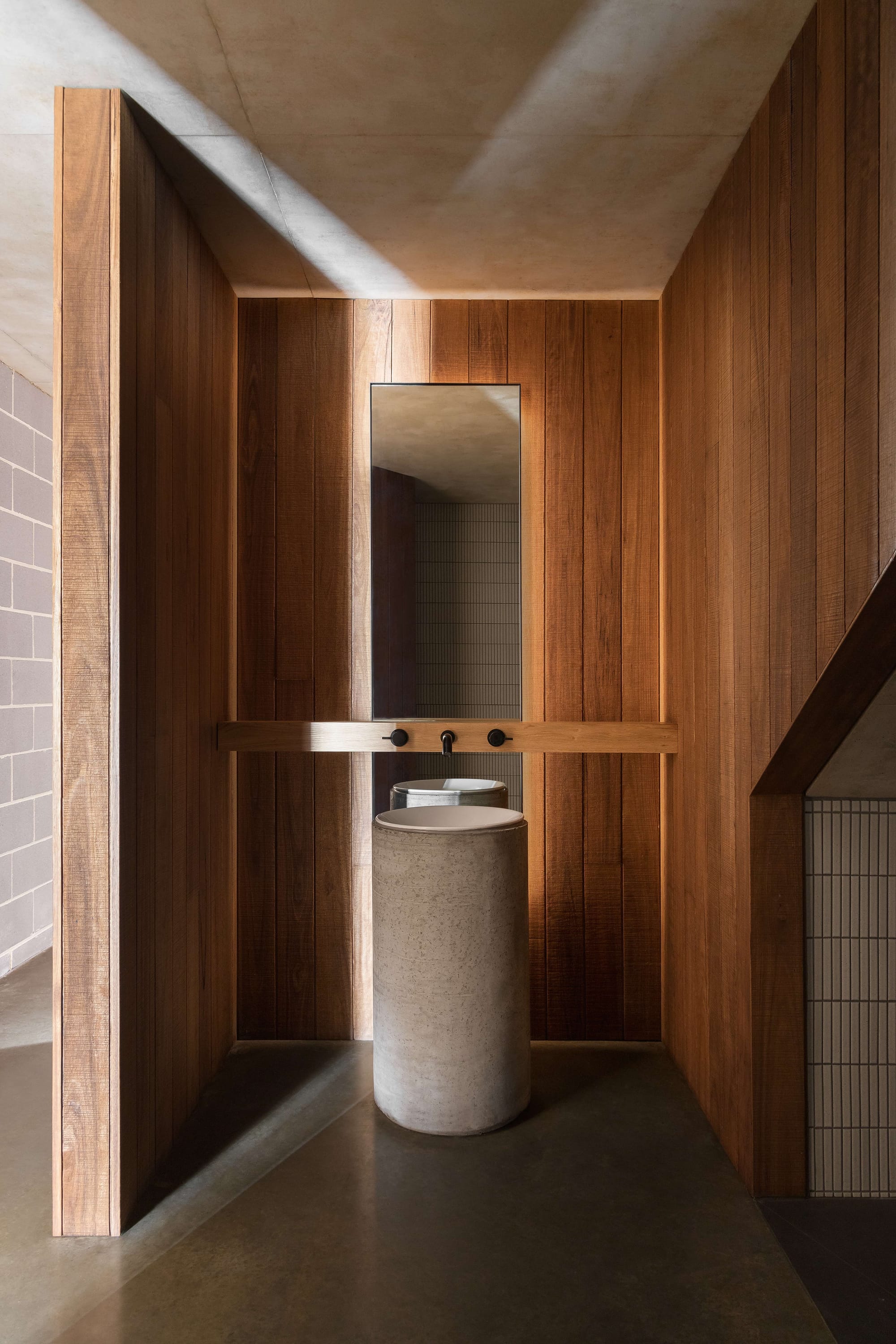 Merricks House by Aktis Architects. Photography by Timothy Kaye. Minimalist bathroom with vertical timber walls, cylindrical concrete basin, wall-mounted tapware, and a tall mirror.
