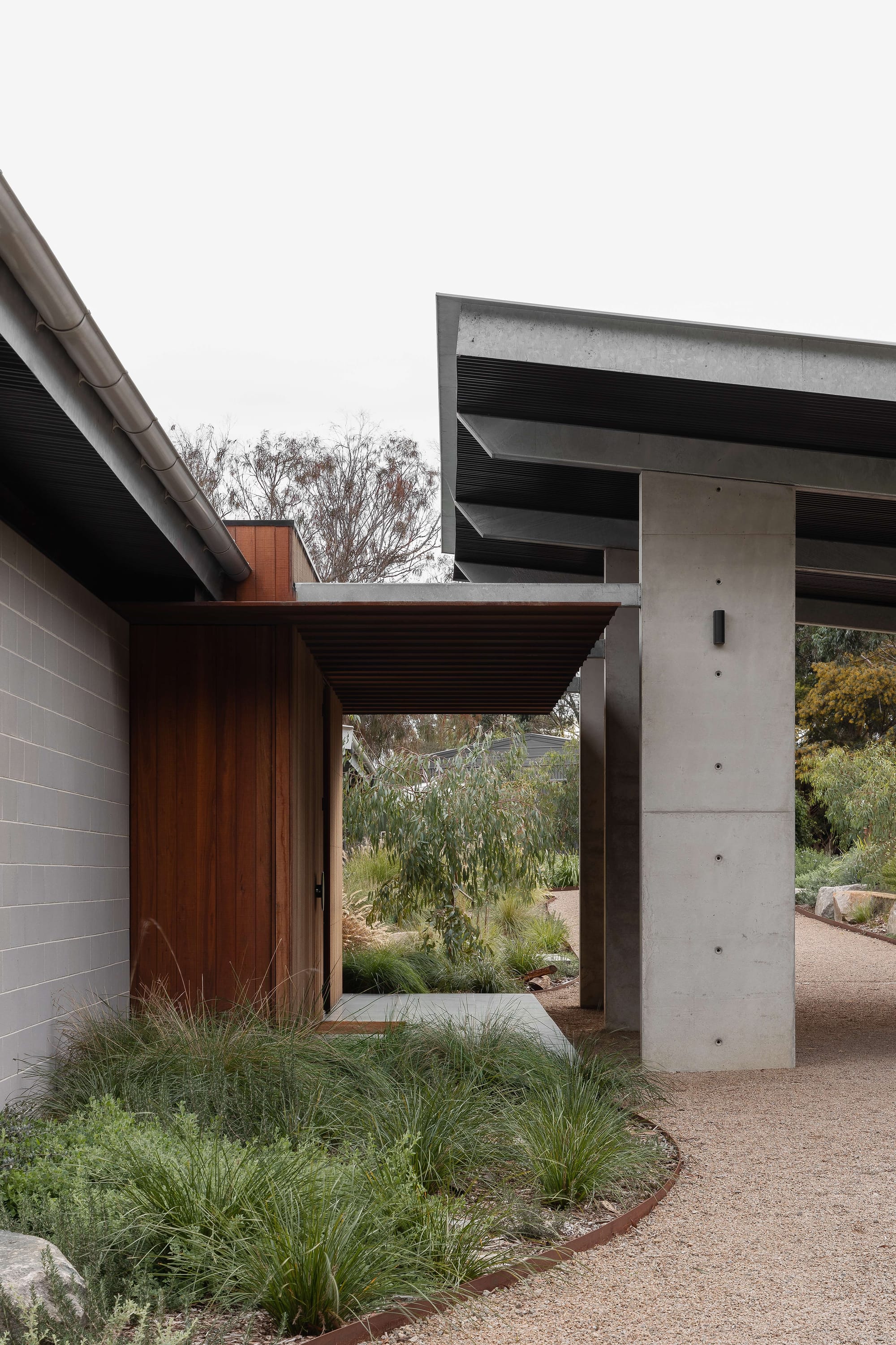 Merricks House by Aktis Architects. Photography by Timothy Kaye. Architectural detail of a modern entry with timber cladding, concrete columns, and steel canopy set within native landscaping.