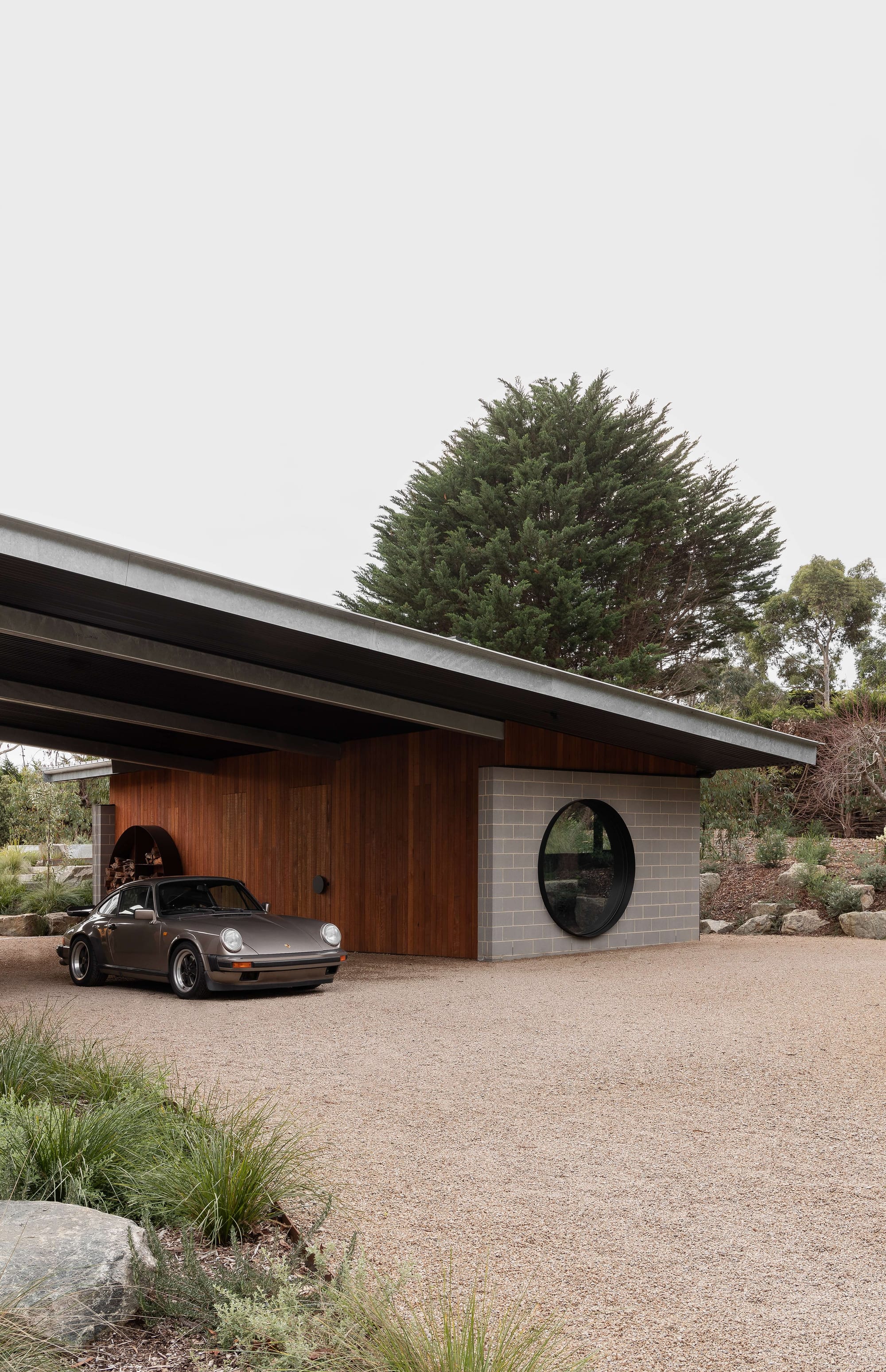 Merricks House by Aktis Architects. Photography by Timothy Kaye. Modern carport with timber and blockwork walls, circular window, and pitched metal roof sheltering a vintage Porsche.