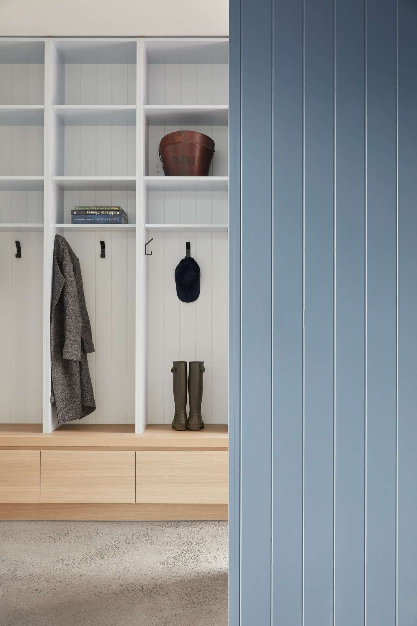 The Unbricked House by Merrylees Architecture. Photography by Tom Ross. Laundry and mud room space with polished concrete flooring, white and timber open-faced cabinetry and hanging space, and sky blue timber clad detailing.