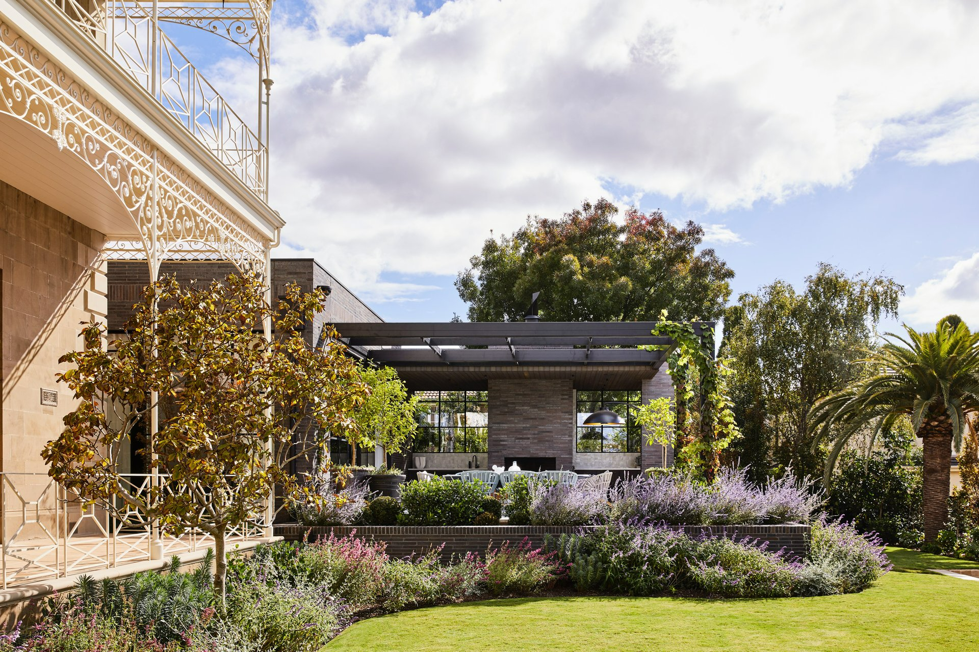 Geelong, Victoria by Myles Baldwin Design. Photographer undisclosed. Geelong, Victoria by Myles Baldwin Design. Photographer undisclosed. Victorian home with colourful gardens and grass alongside dark coloured patio.