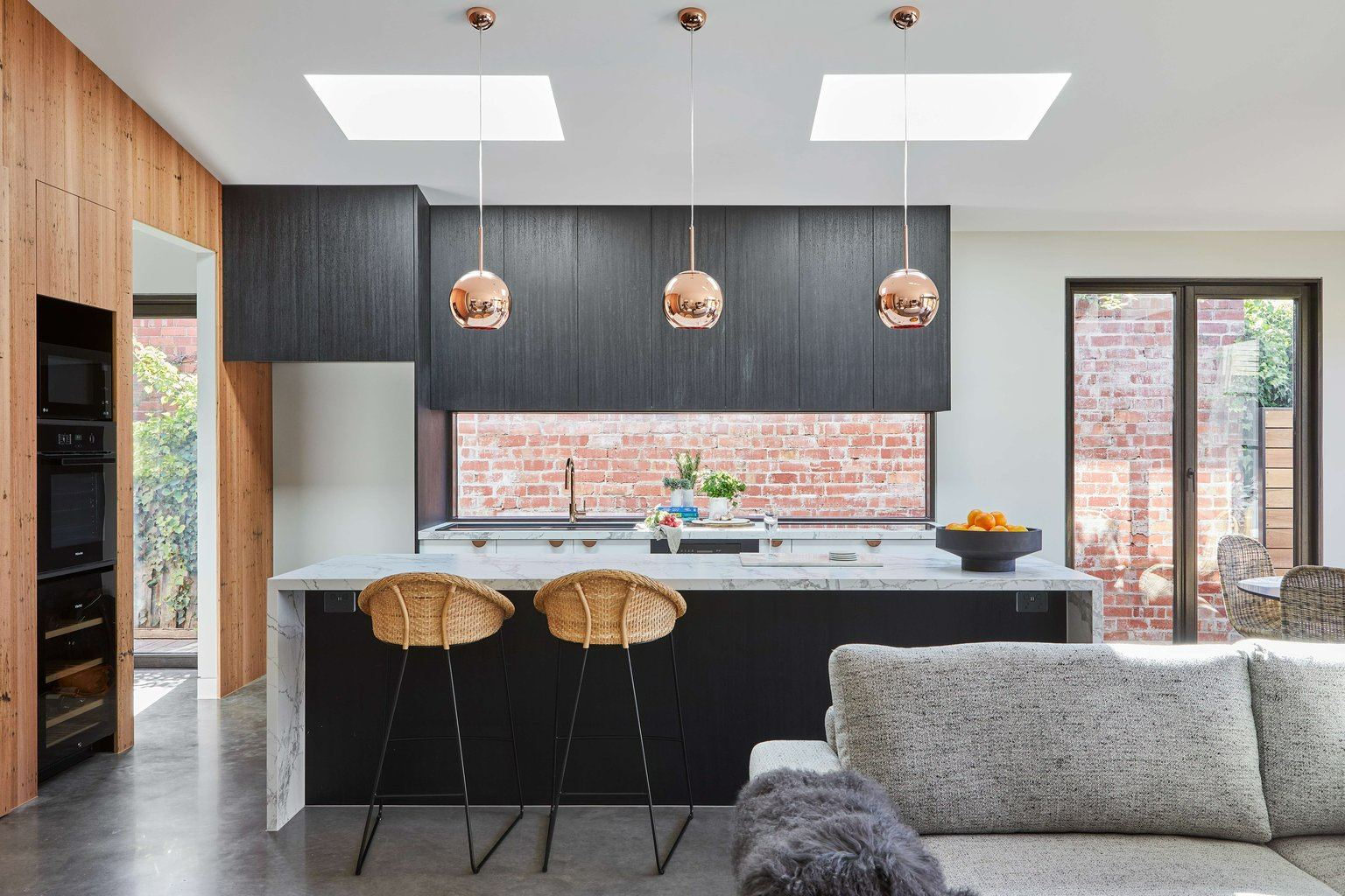 Glen Iris Home by Samuel Architecture. Photography by Dave Kulesza. Kitchen with black cabinetry, white marble benchtop and glass splashback overlooking brick wall.