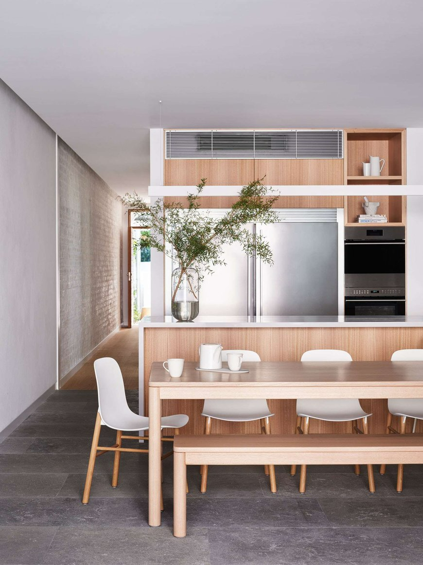 Manly 22 by Watershed Architects. Photography by Alicia Taylor Photography. Open plan kitchen and dining space with dark grey floor tiles, timber table and cabinetry and silver fixtures.