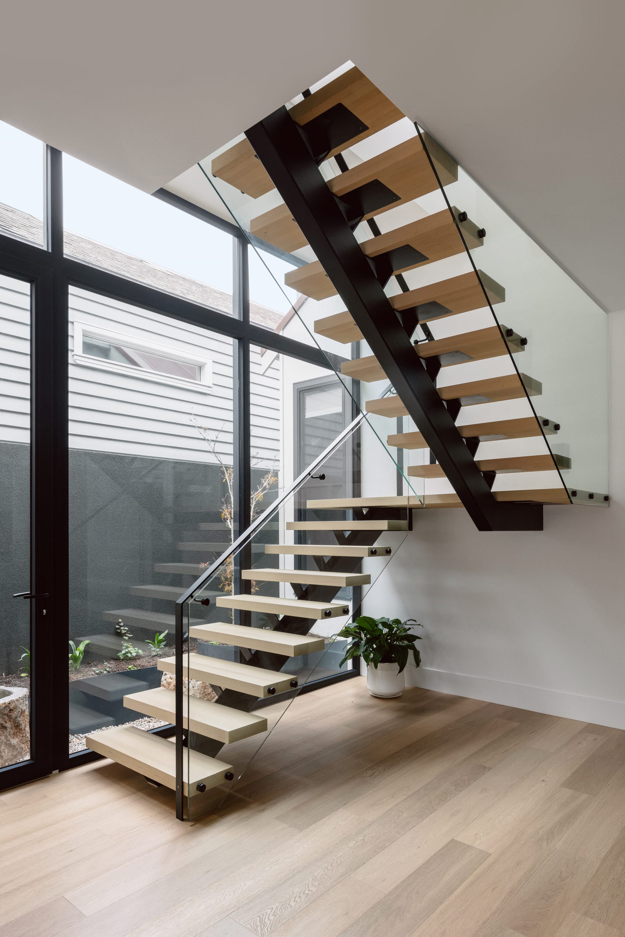 Auburn Residence by Chan Architecture. Photography by Elise Scott. Glass and timber staircase in open plan space with timber flooring and black framed glass walls.