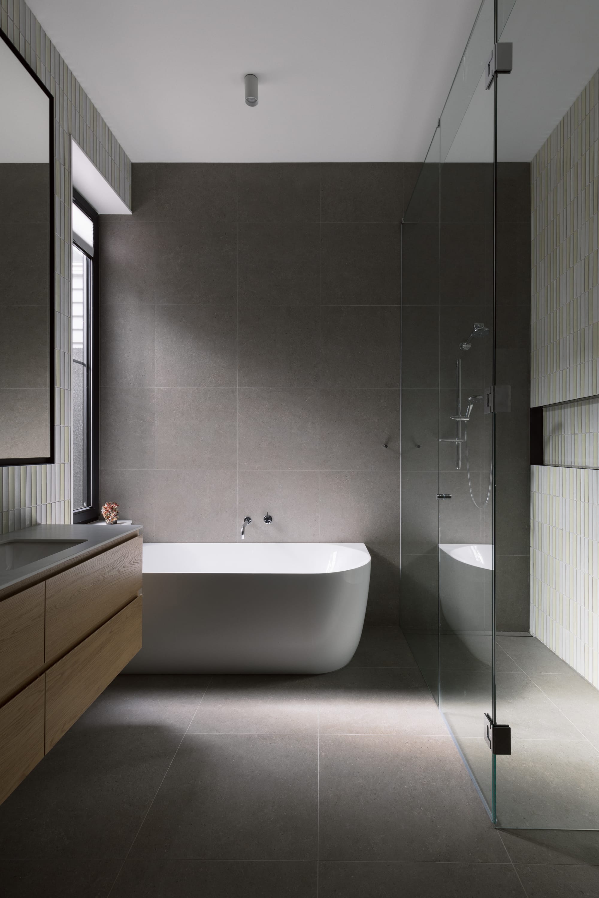 Auburn Residence by Chan Architecture. Photography by Elise Scott. Bathroom with freestanding white bath, grey floor and wall tiles and a timber floating cabinet.