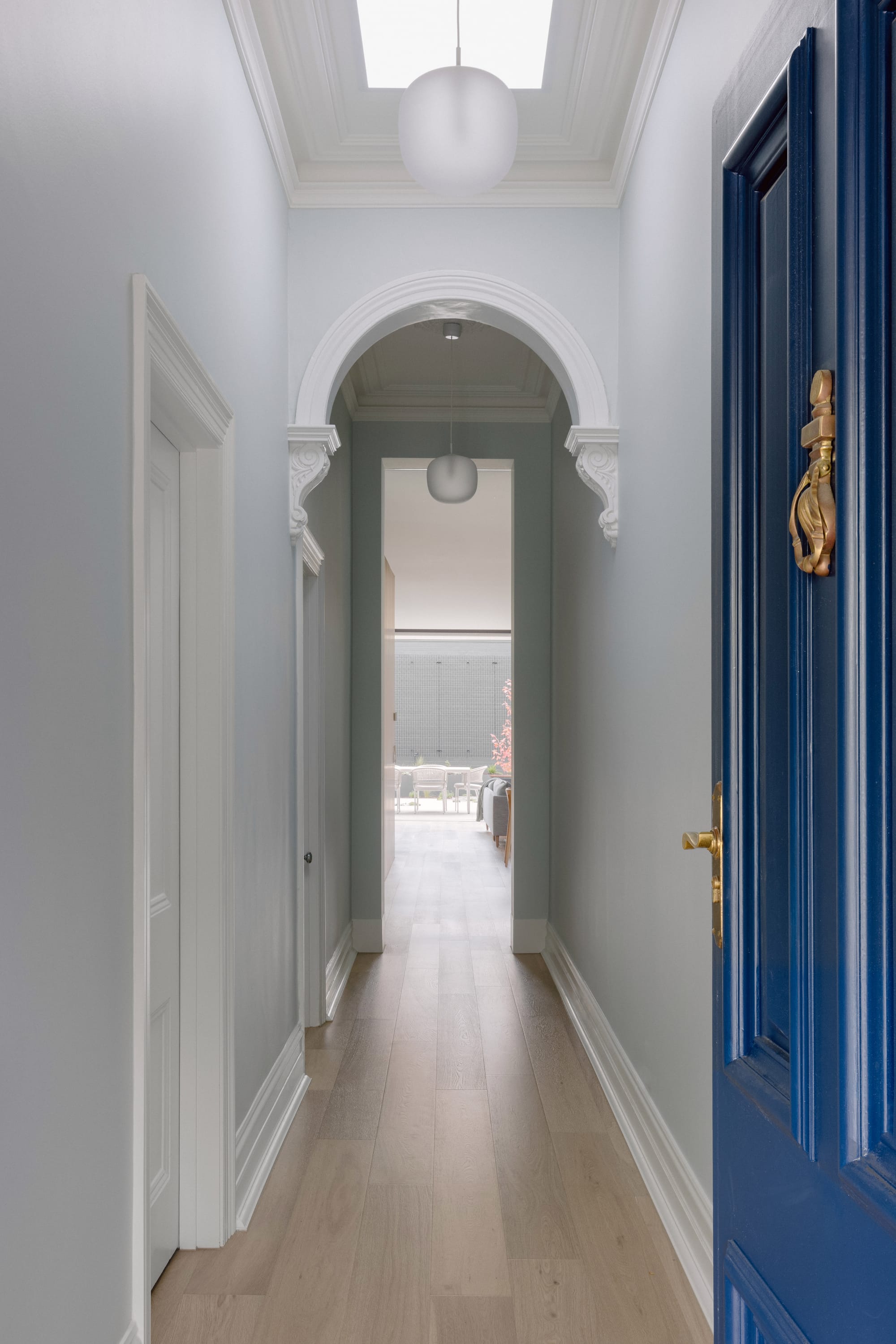 Auburn Residence by Chan Architecture. Photography by Elise Scott. Hallway of home with electric blue front door, timber flooring, grey walls and white details.