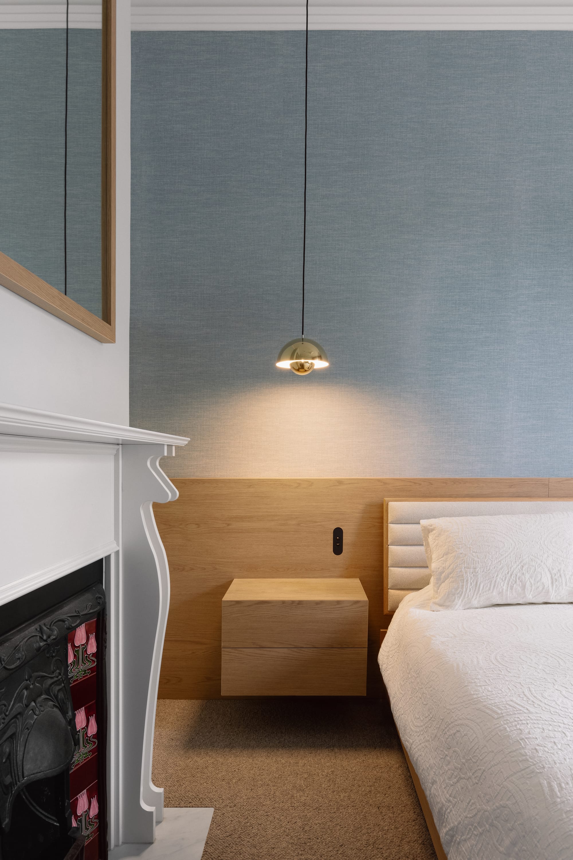 Auburn Residence by Chan Architecture. Photography by Elise Scott. Bedroom with original white fireplace, integrated timber headboard, blue wallpaper and white patterned bedding.