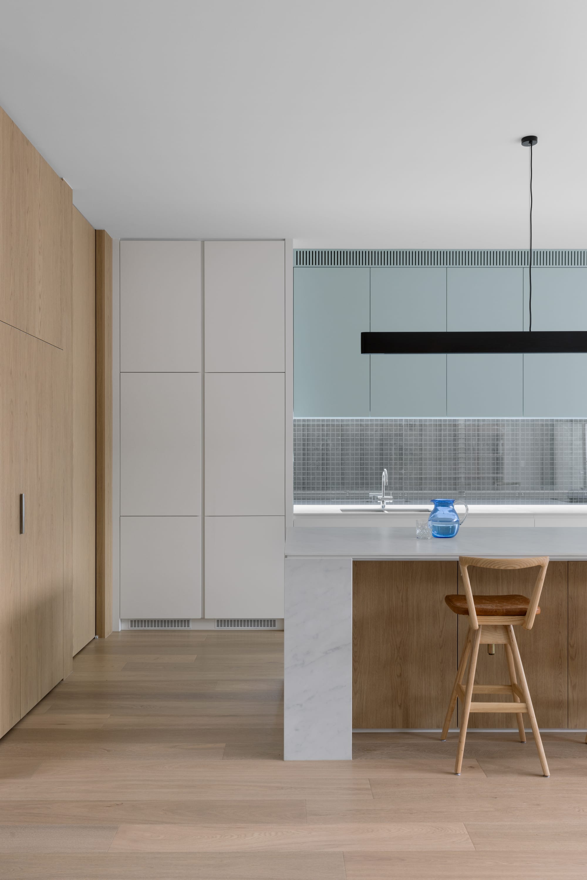 Auburn Residence by Chan Architecture. Photography by Elise Scott. Kitchen with pale timber flooring and joinery, with a white marble benchtop and light blue overhead cabinetry.