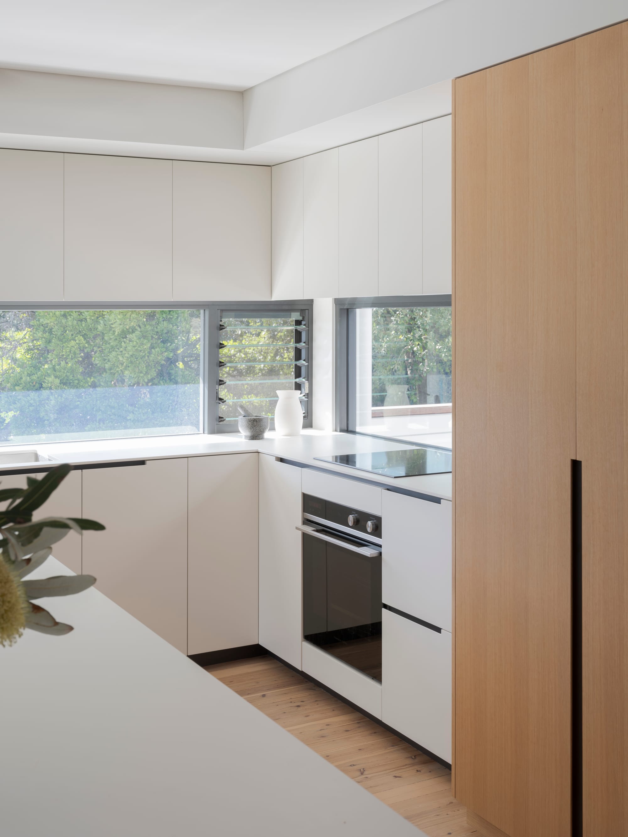 Three Points House by BIJL Architecture. Photography by Tom Ferguson. Close-up of sleek modern kitchen featuring white cabinetry, integrated appliances, and corner windows with garden views.