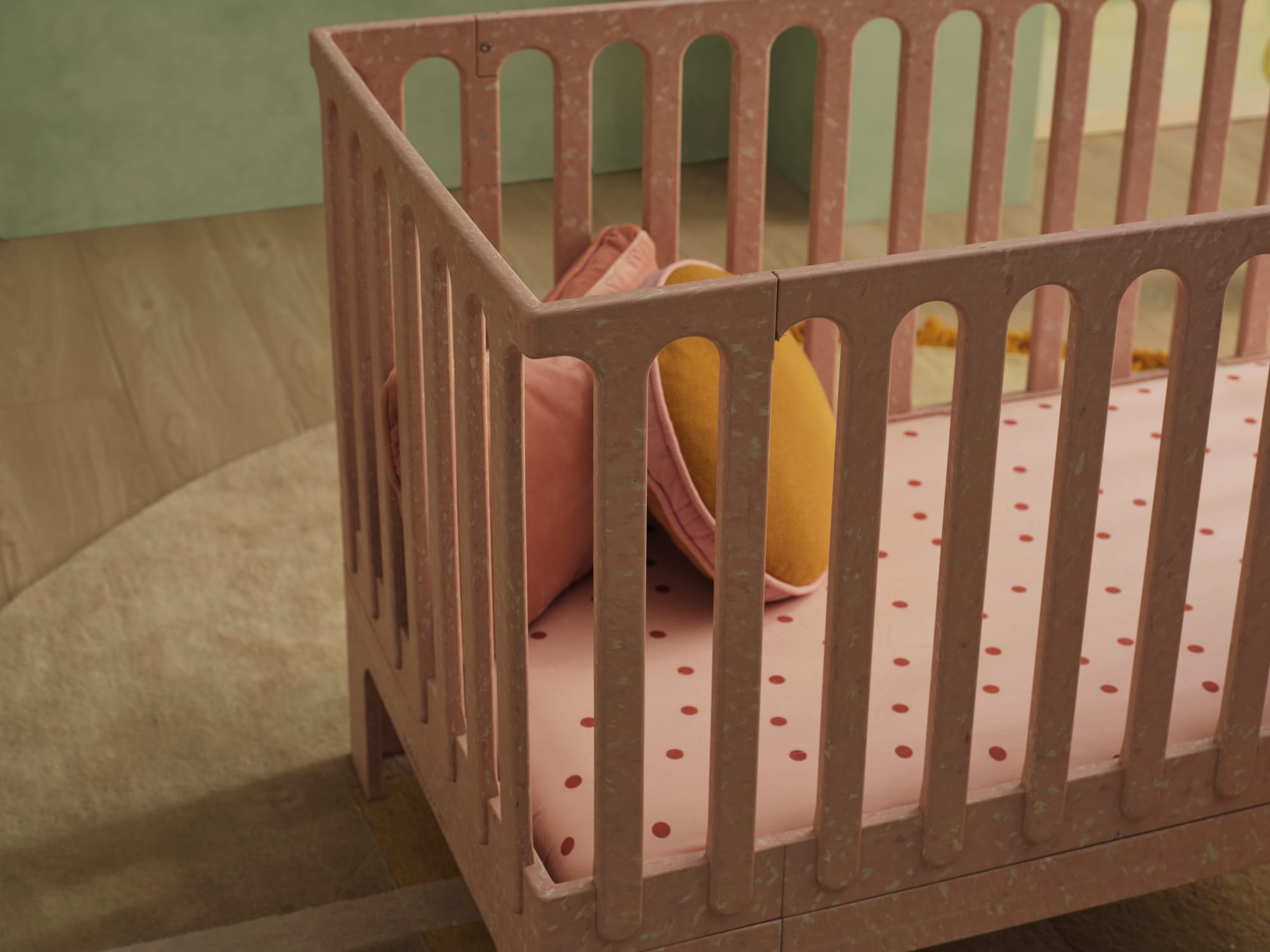 Archie Cot by Seena x Defy in Dusty Rose. Close up of pink cot with pink and red polka dot mattress cover, and pink and yellow cushions.