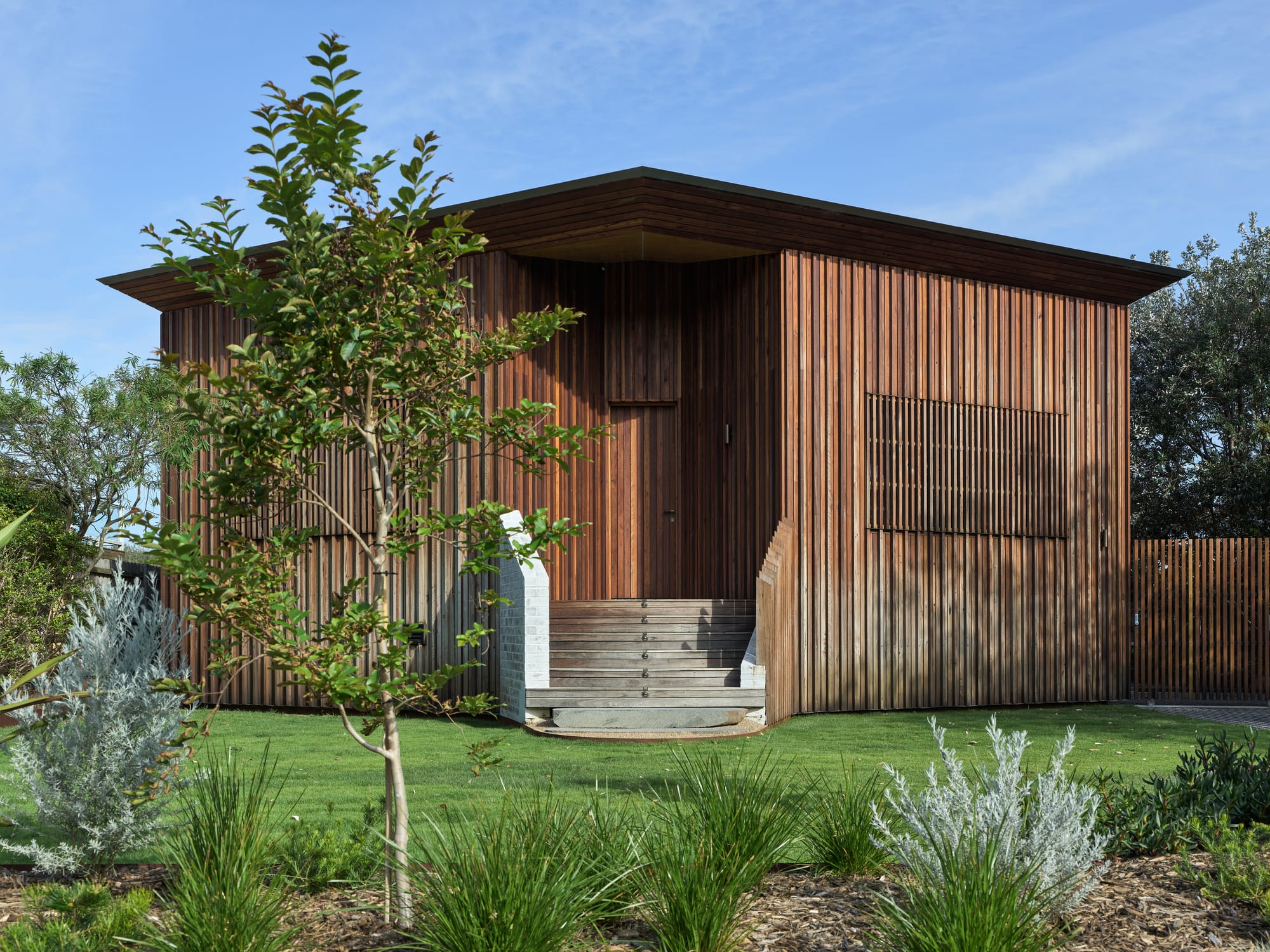 Cake House by Alexander Symes Architect. Photography by Barton Taylor. Street view of small timber clad house with front steps, timber roof and green grass front yard.