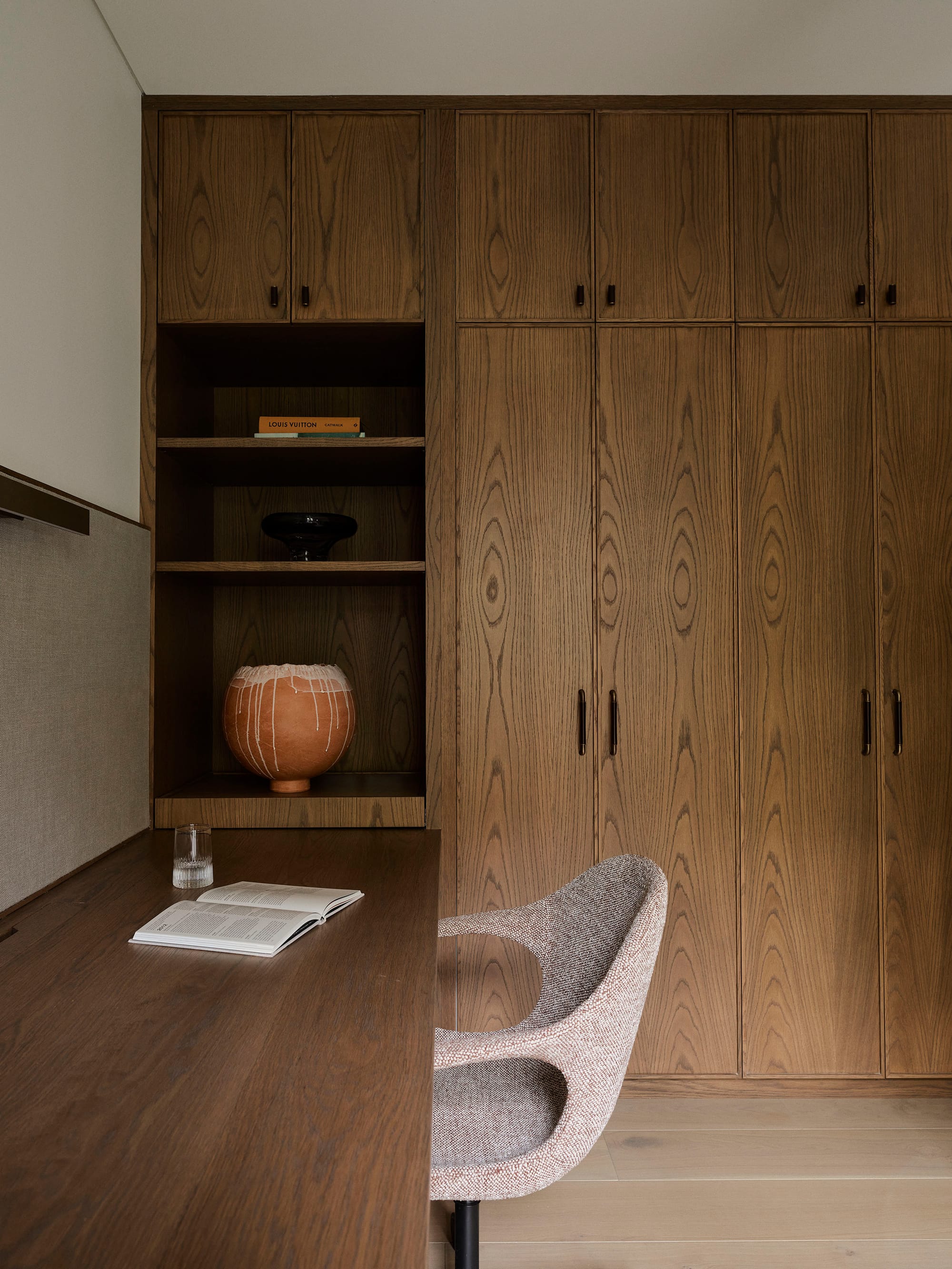 Bundarra Penthouse by Marylou Sobel Interior Design. Photography by Anson Smart. Office space with full height integrated timber cabinetry, storage and desk, with light timber walls, cream wallpaper and grey office chair.