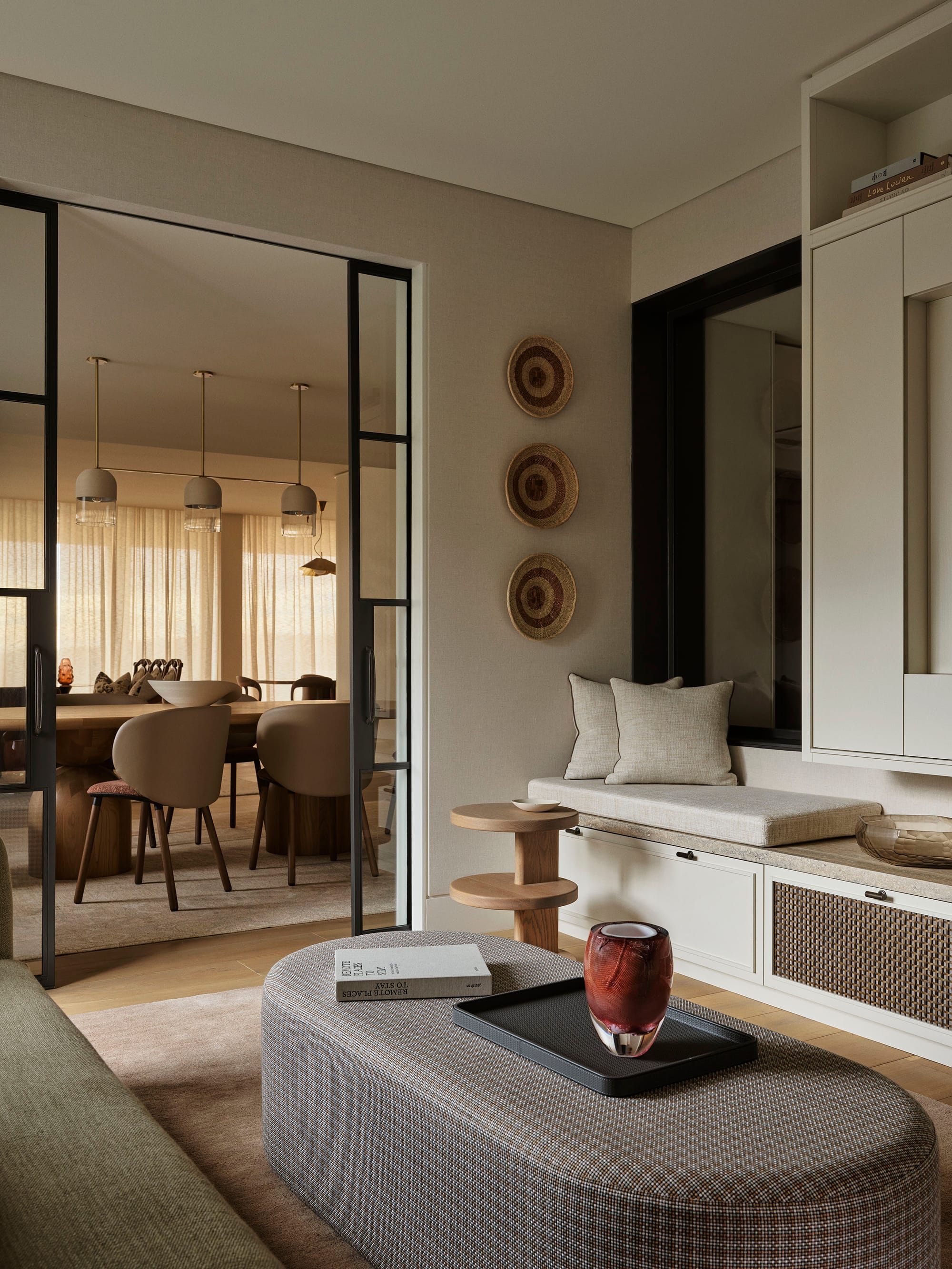 Bundarra Penthouse by Marylou Sobel Interior Design. Photography by Anson Smart. Living space with white cabinetry, fabric oval coffee table and glass archway looking into dining space.