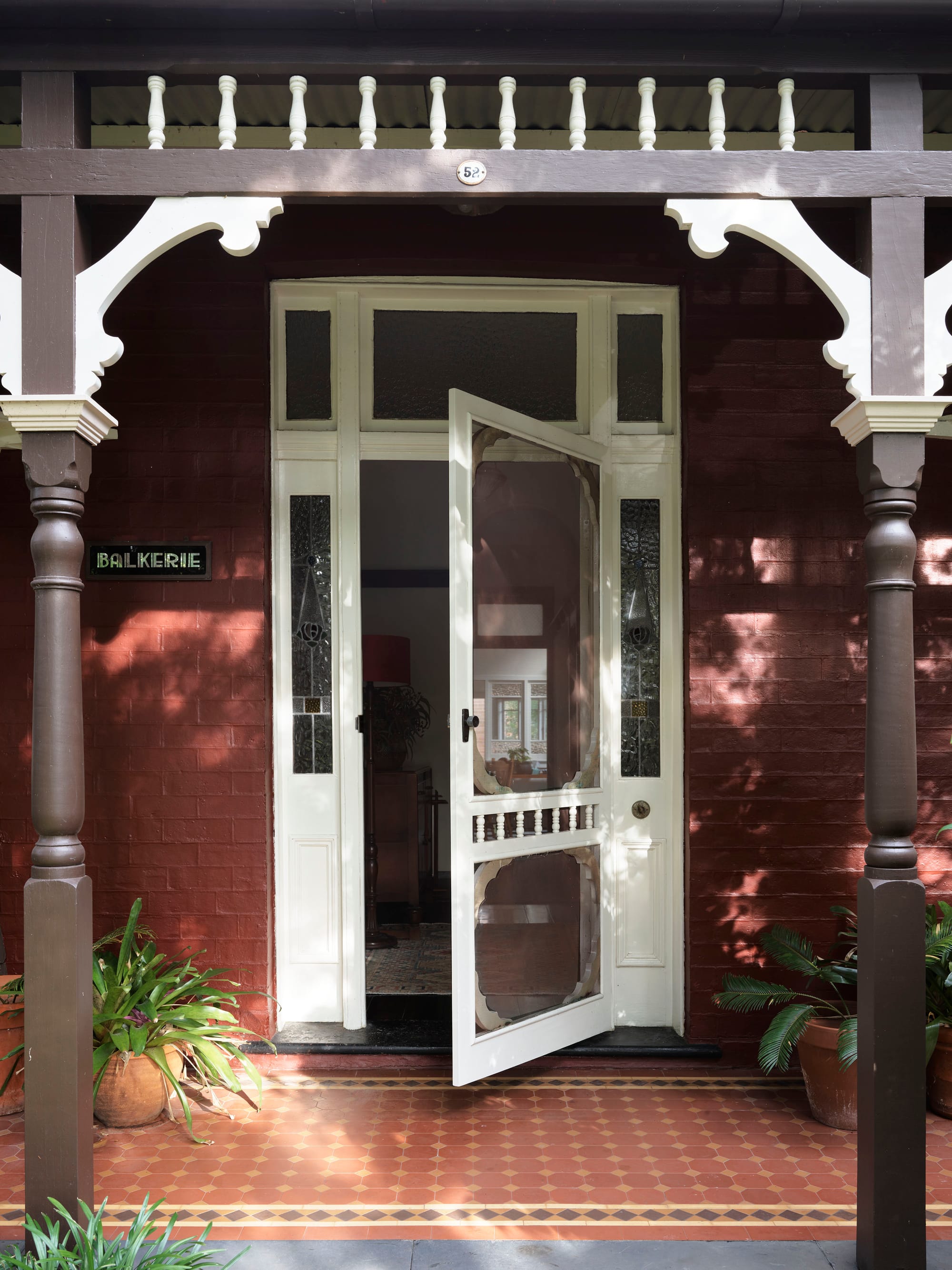 Ferris Street by Marylou Sobel Interior Design. Photography by Anson Smart. Exterior entrance and patio with tiled mosaic flooring, white door with leadlight side windows and red brick exterior walls.