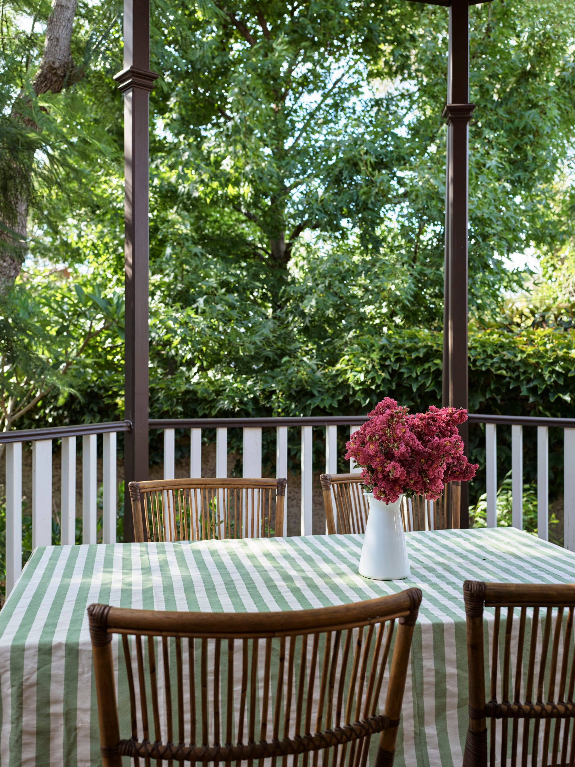 Ferris Street by Marylou Sobel Interior Design. Photography by Anson Smart. Outdoor dining area with striped green tablecloth, timber dining chairs and white and timber balustrade overlooking garden.