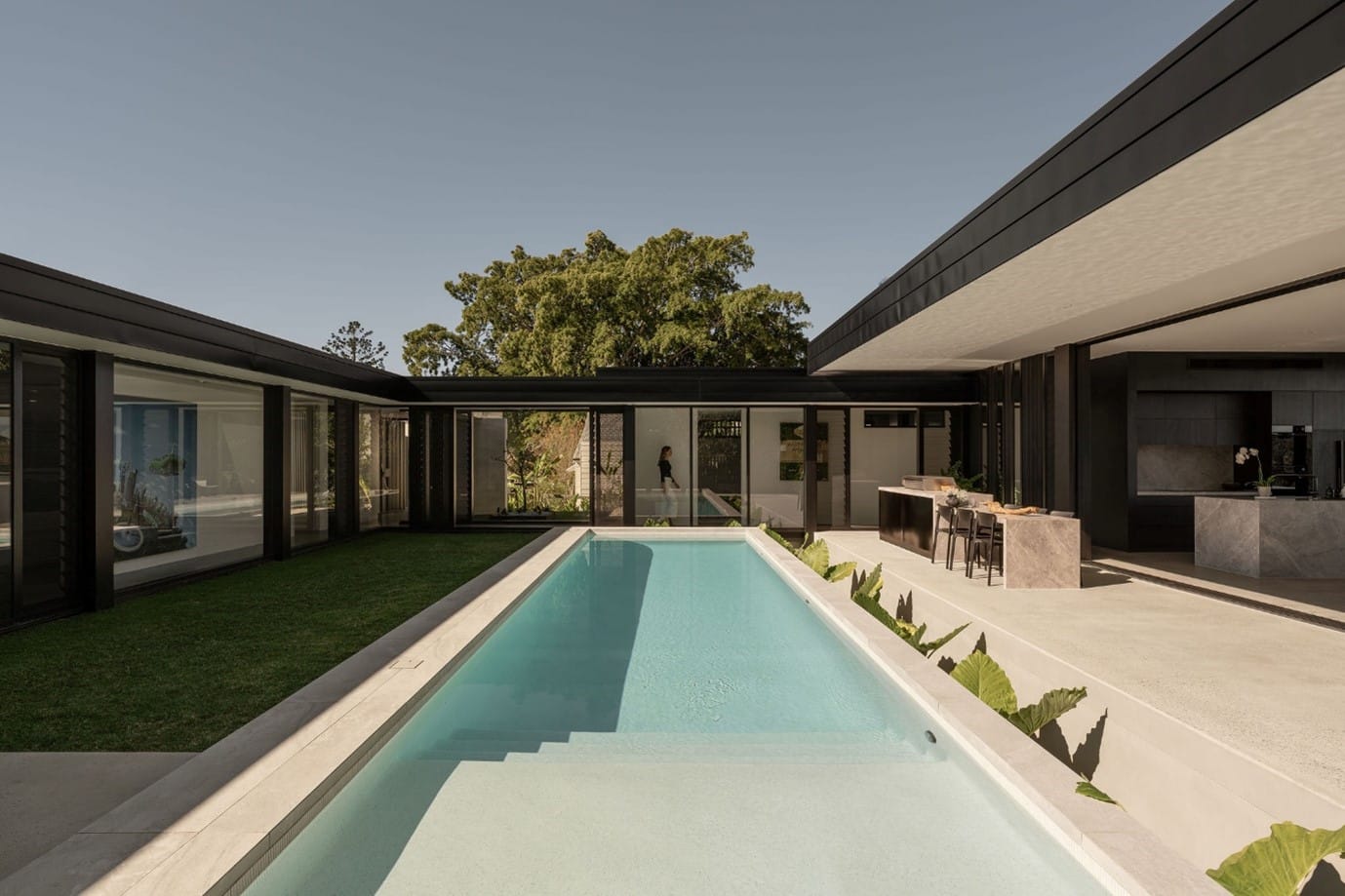 The River House, Indooroopilly by Sarah Waller Architecture. Photography by Alyne Media. Light pool lap pool in centre courtyard of home, with black-framed windows and doors connecting outdoors to the inside of the house.