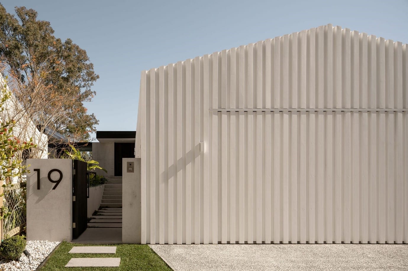 The River House, Indooroopilly by Sarah Waller Architecture. Photography by Alyne Media. Facade of residential home with timber clad garage in white, with stairs to front door on the left.