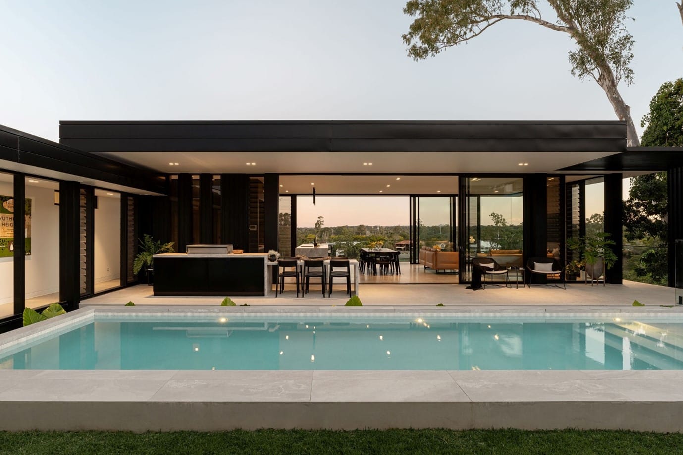 The River House, Indooroopilly by Sarah Waller Architecture. Photography by Alyne Media. Pool in front of outdoor patio, with black-framed glass windows and doors in the background.
