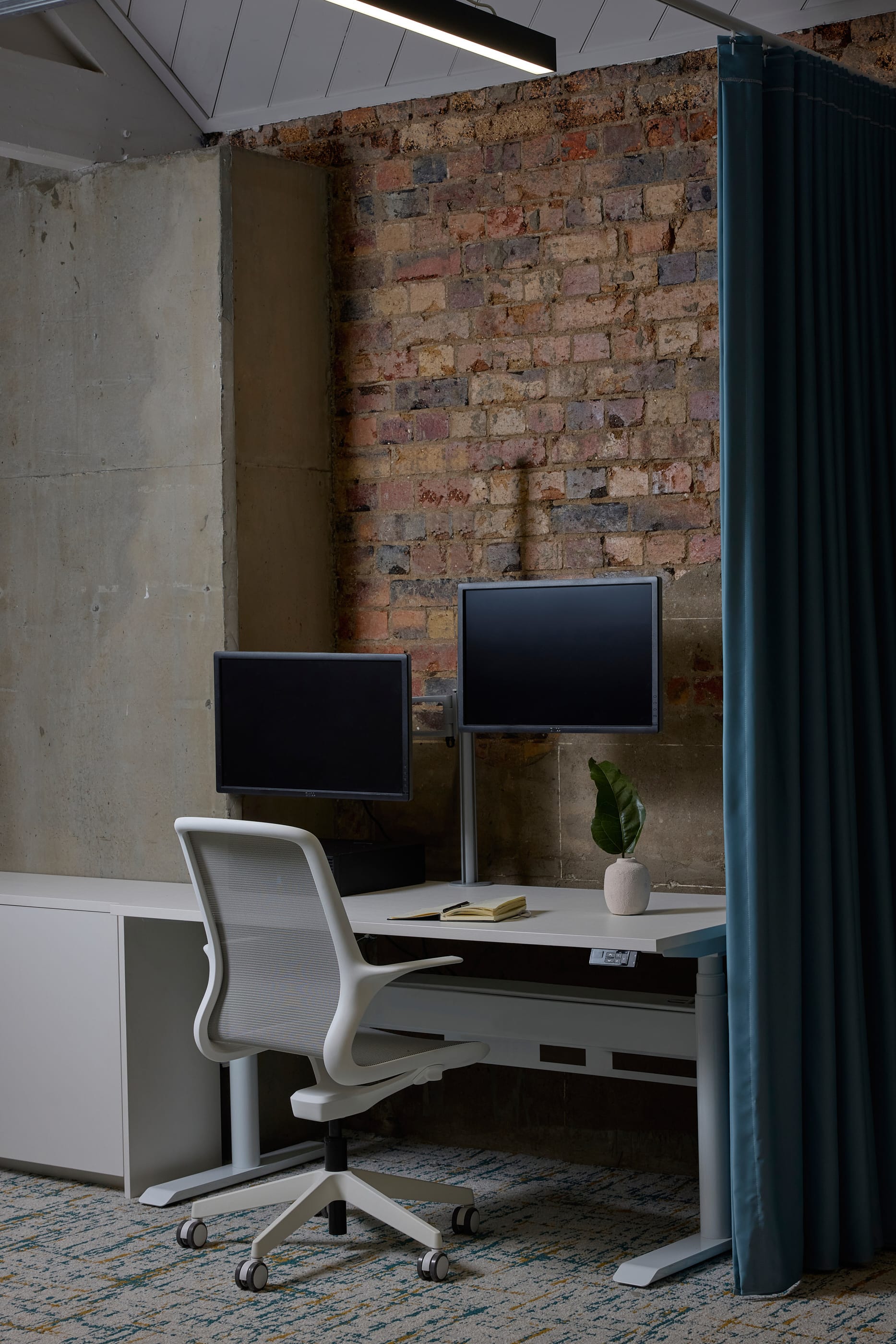 Project Kalakal by M&E Interiors. Office set up with white desk and chair, two monitor screens and exposed brick walls.