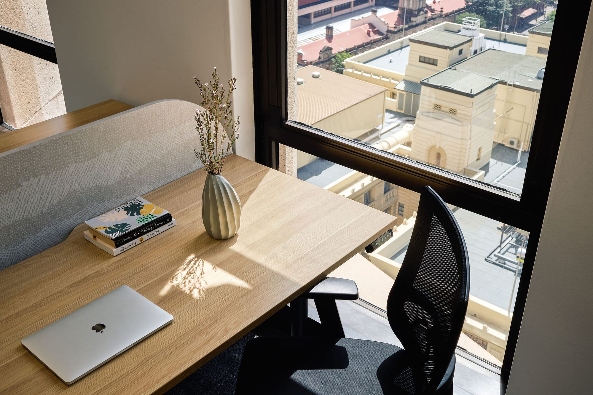 Project Kubo by M&E Interiors. At home office set up with small timber desk with black chair and laptop, next to full height window overlooking city views below.