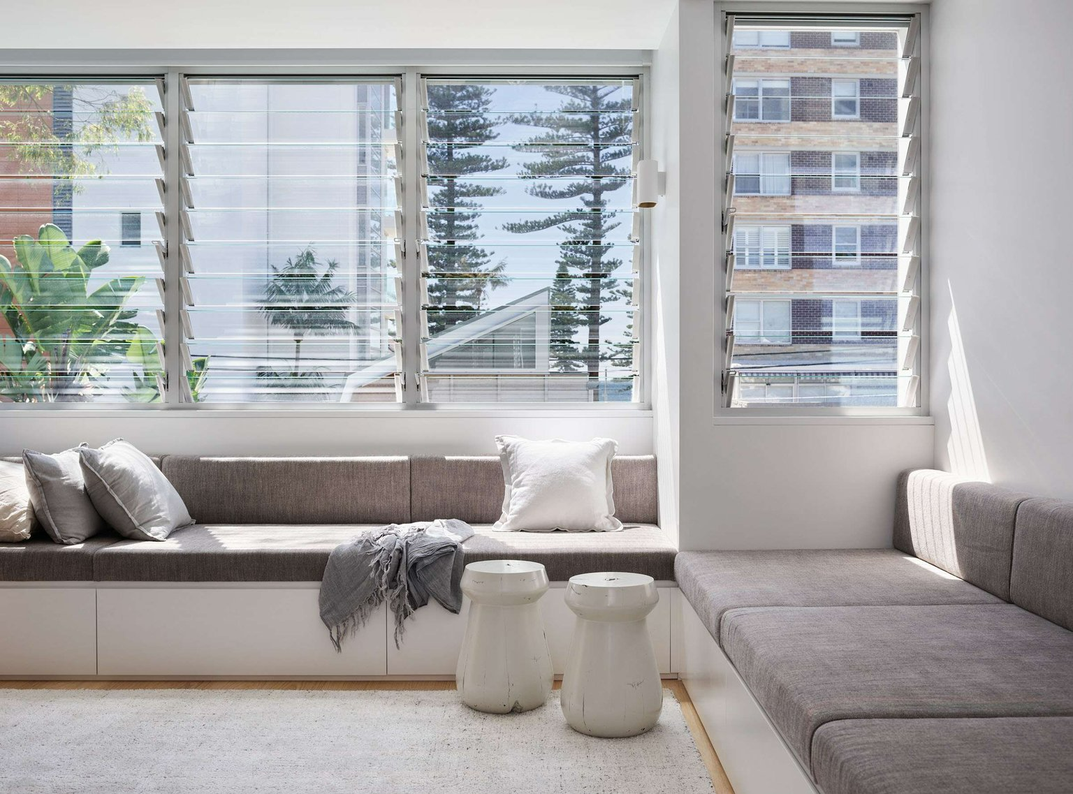 Manly 22 by Watershed Architects. Photography by Alicia Taylor Photography. Living space with louvre glass shutters overlooking city views, with a built-in grey and white window bench.  