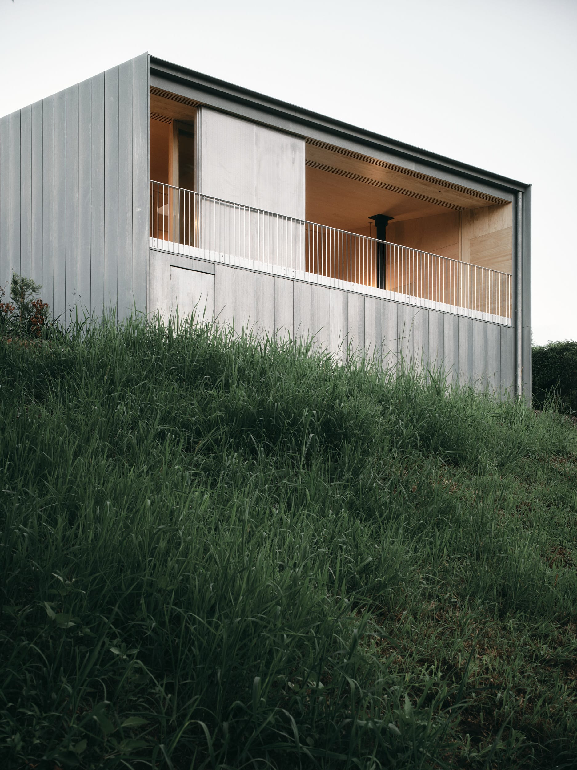 Mapleton House by Atelier Chen Hung. Photography by David Chatfield. Double storey home with zinc exterior and balcony on top of grassy hill.