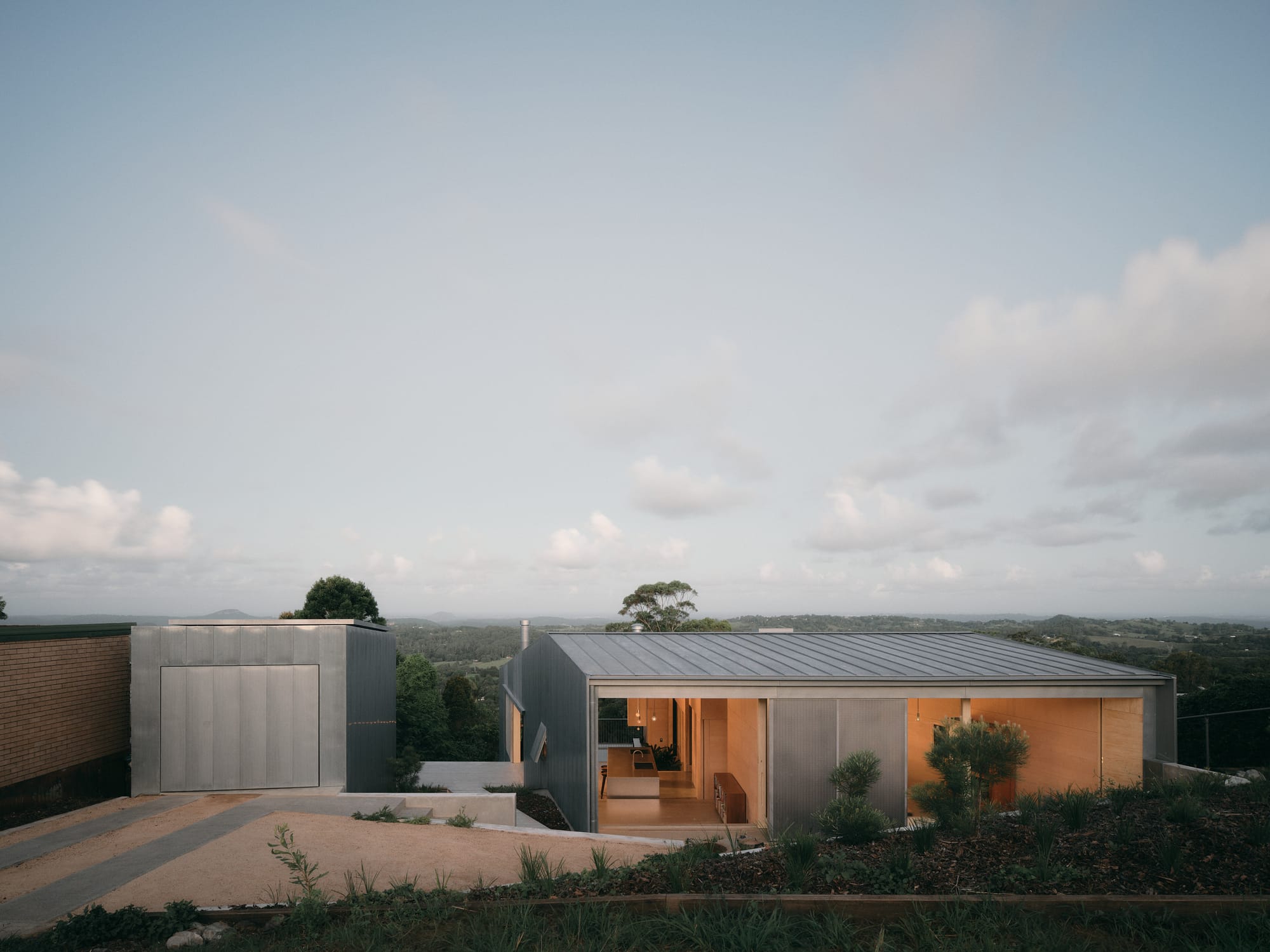 Mapleton House by Atelier Chen Hung. Photography by David Chatfield. Aluminium home with large openings in hilly landscape with heavy foliage.
