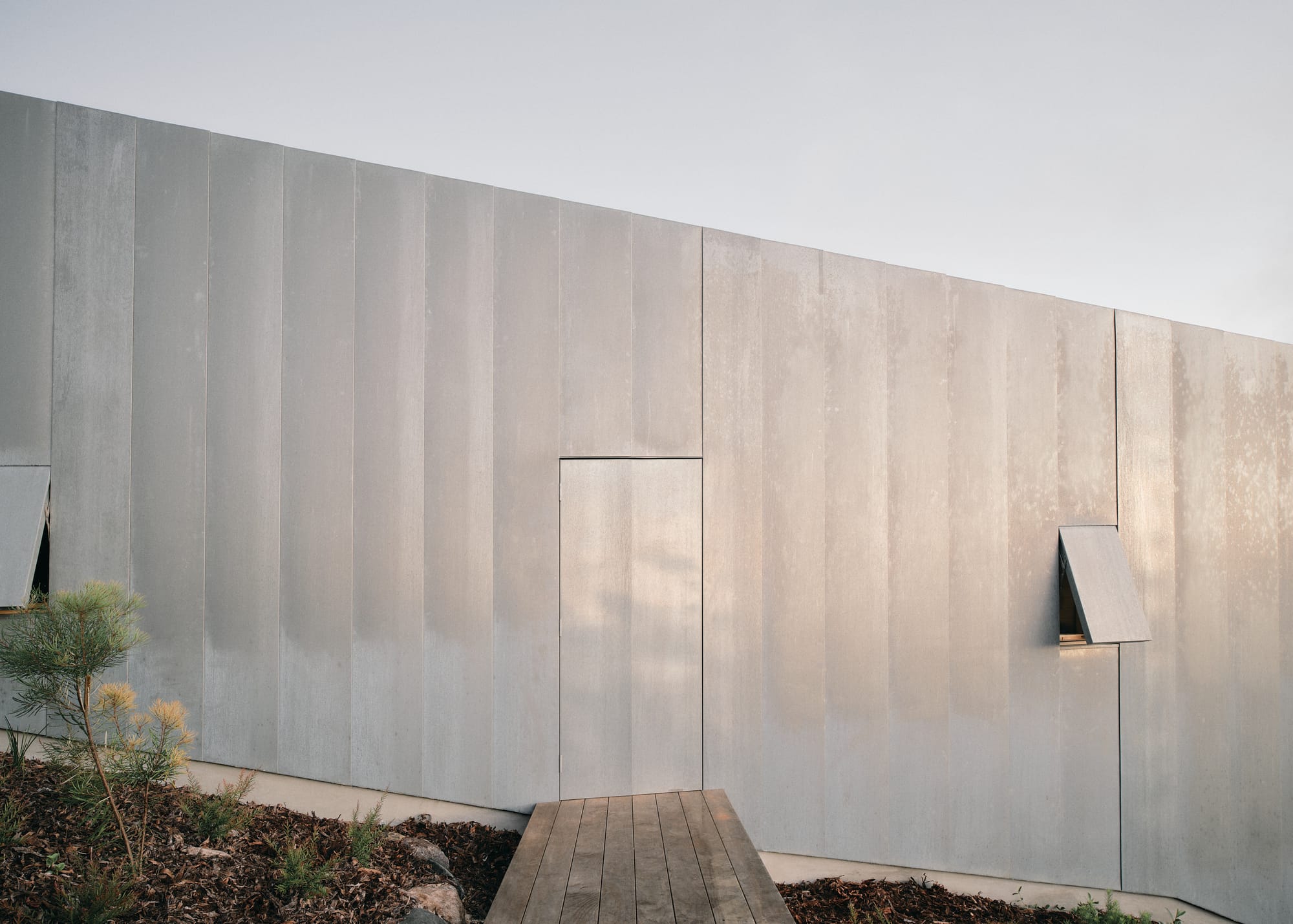 Mapleton House by Atelier Chen Hung. Photography by David Chatfield. Exterior facade of zinc-clad home, angled on the hillside with sleek doors and windows.