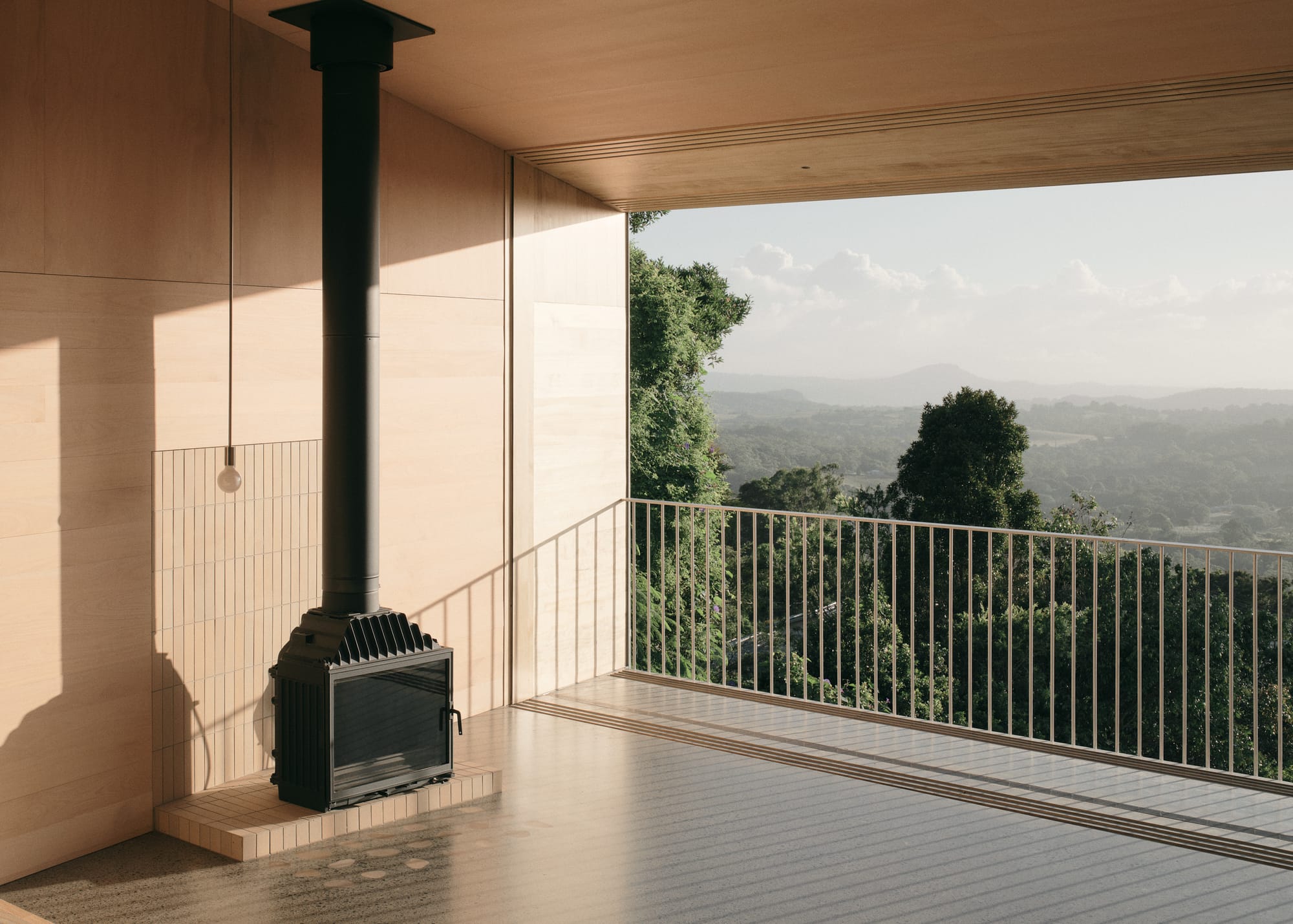 Mapleton House by Atelier Chen Hung. Photography by David Chatfield. Black fireplace in room with concrete floors, timber walls and large balcony views over mountains.