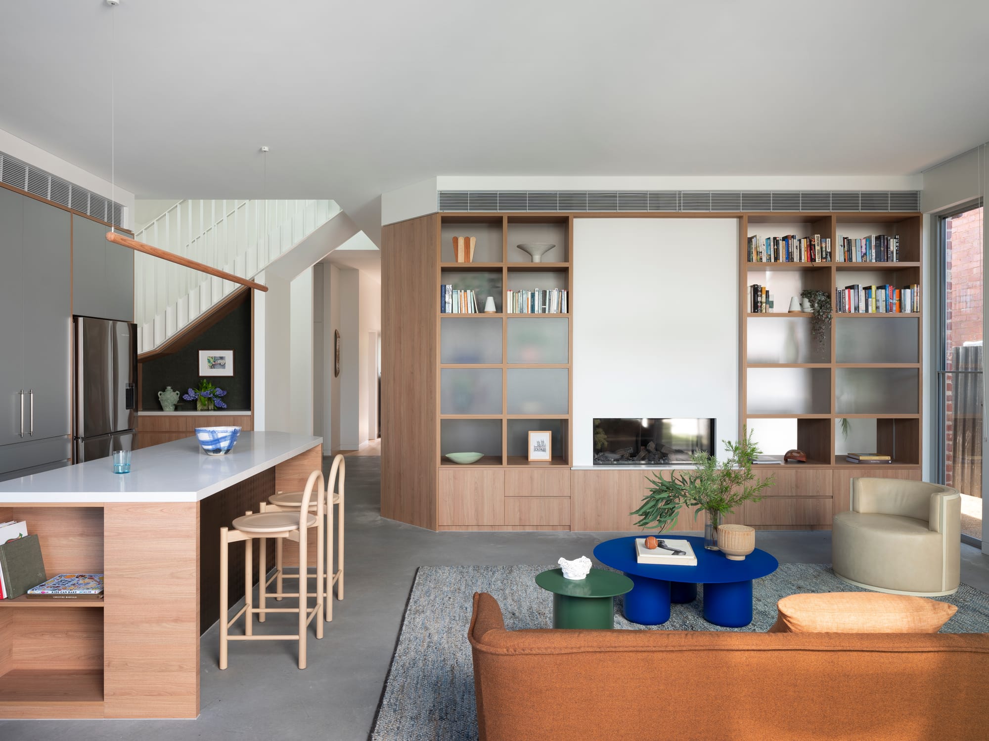 Merrilands by BIJL Architecture. Photography by Tom Ferguson. Open plan liviing and kitchen space with terracotta coloured couch, open-face storage and timber island bench.