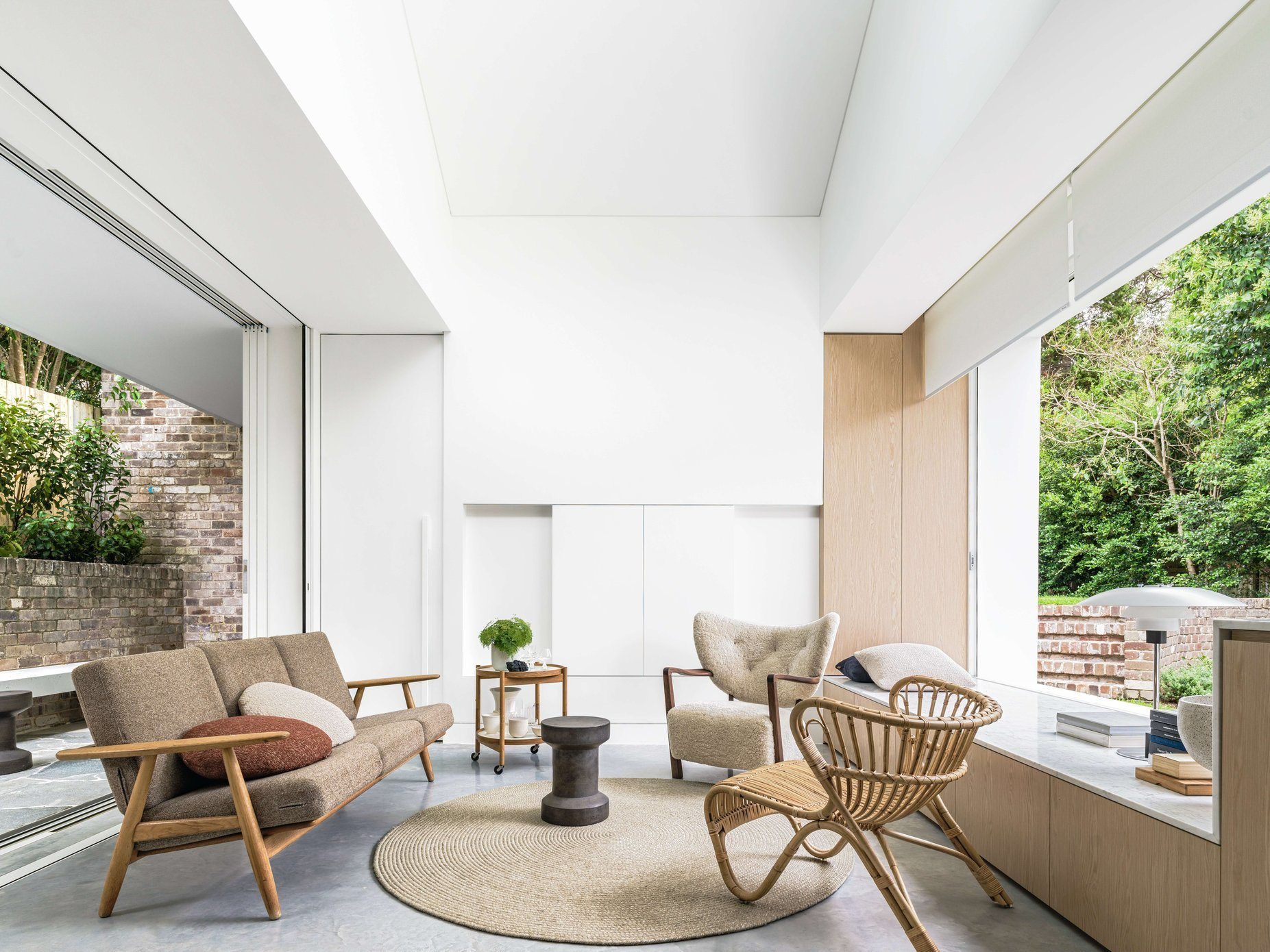 A House for Grandma by Brcar Morony Architecture. Photography by Justin Alexander. Living space with concrete floors, timber and wicker furnishings and round jute rug.