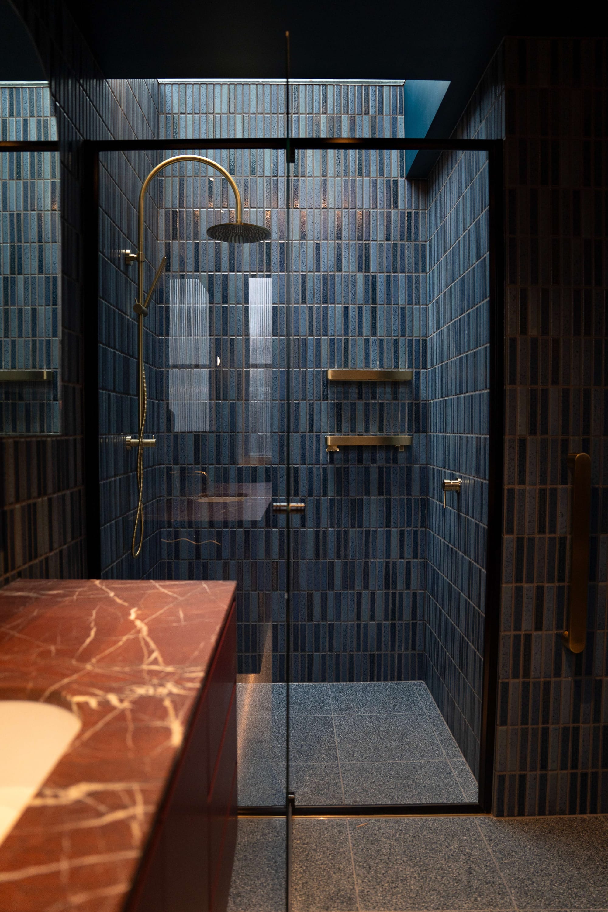 Murrumbeena by PREM.BUILT. Image copyright of Prem.Built. Shower with floor-to-ceiling blue mosaic tiled walls, gold tapware, blue floor tiles and a glass shower screen. 