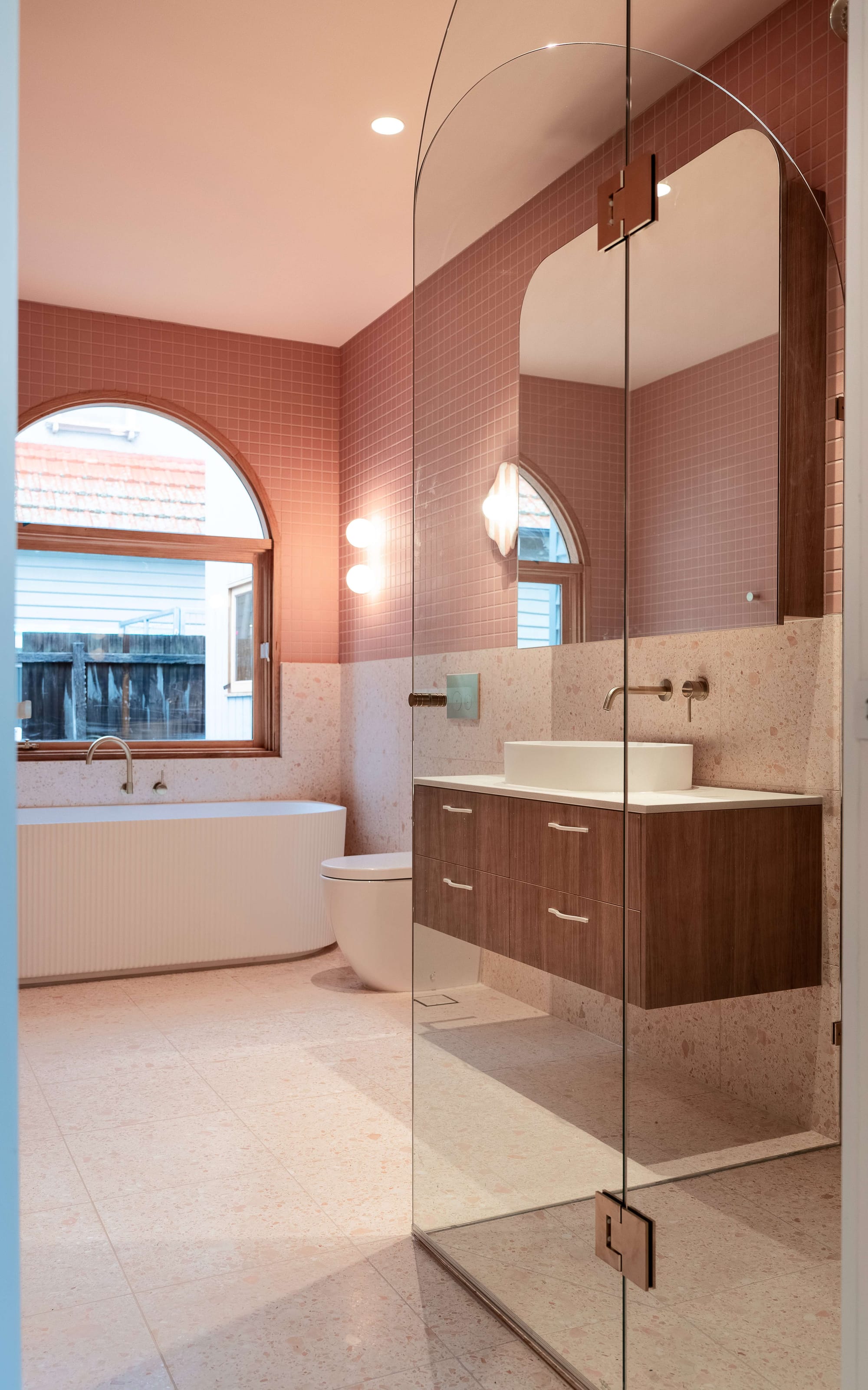 Murrumbeena by PREM.BUILT. Image copyright of Prem.Built. Bathroom with glass shower screen, timber cabinetry, pink mosaic tiles and terrazzo flooring. 