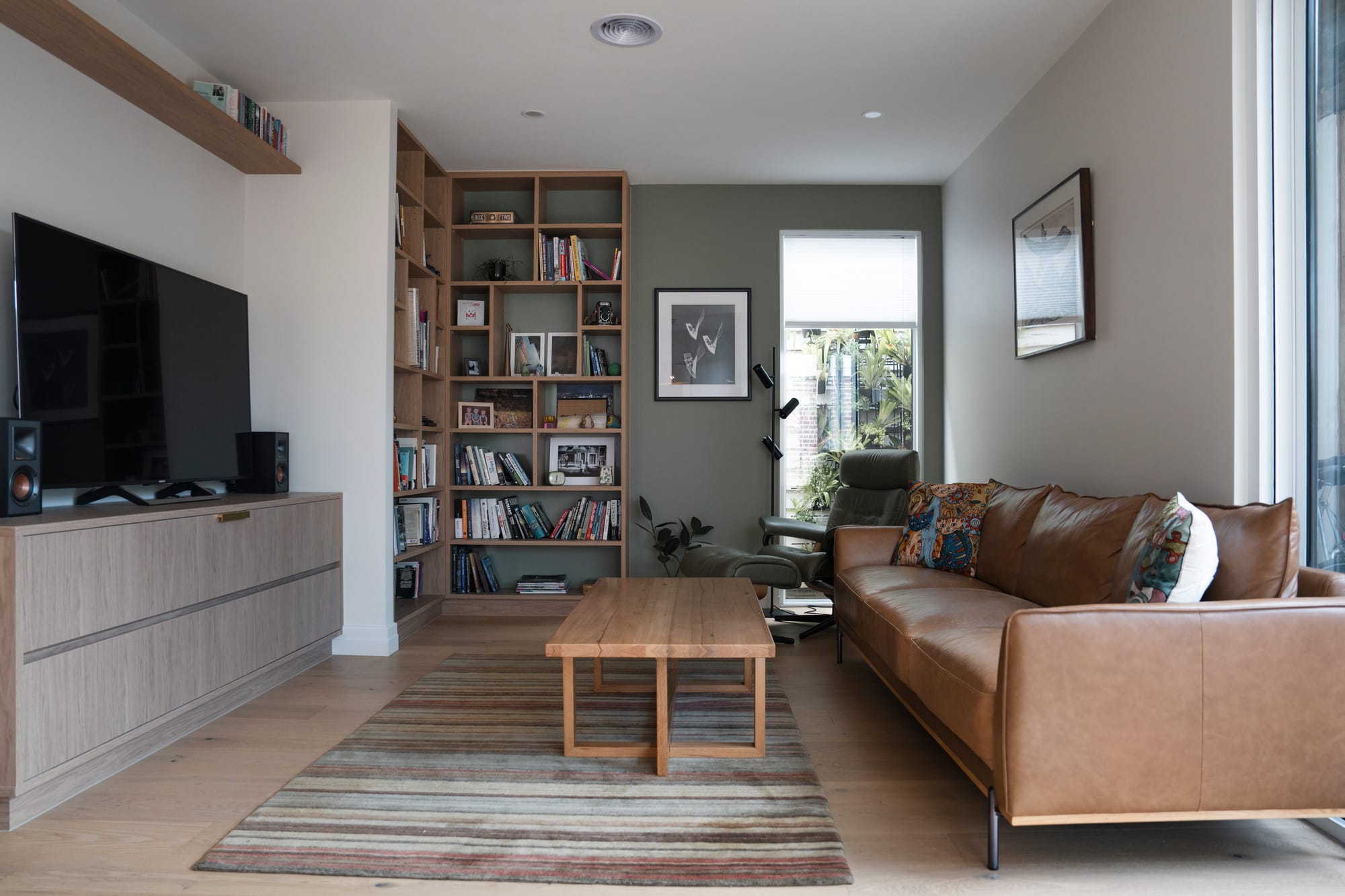 Port Melbourne 2.0 by PREM.BUILT. Image copyright of Prem.Built. Living space with brown leather couch, sage green walls, timber bookshelf and coffee table. 