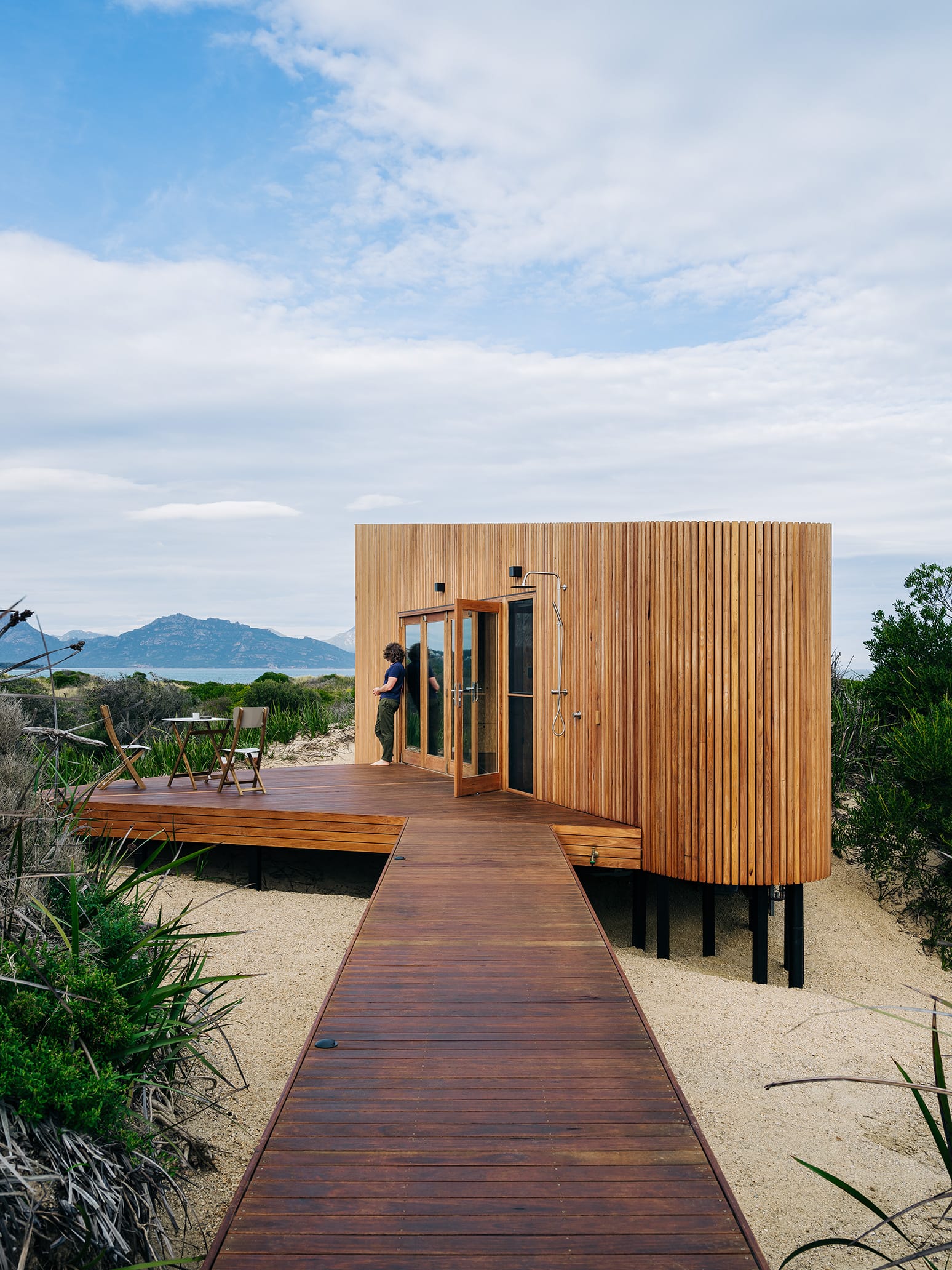 Studio Tasmania. Photography by Adam Gibson. Boardwalk over sand leading to timber clad beach pod with timber deck.