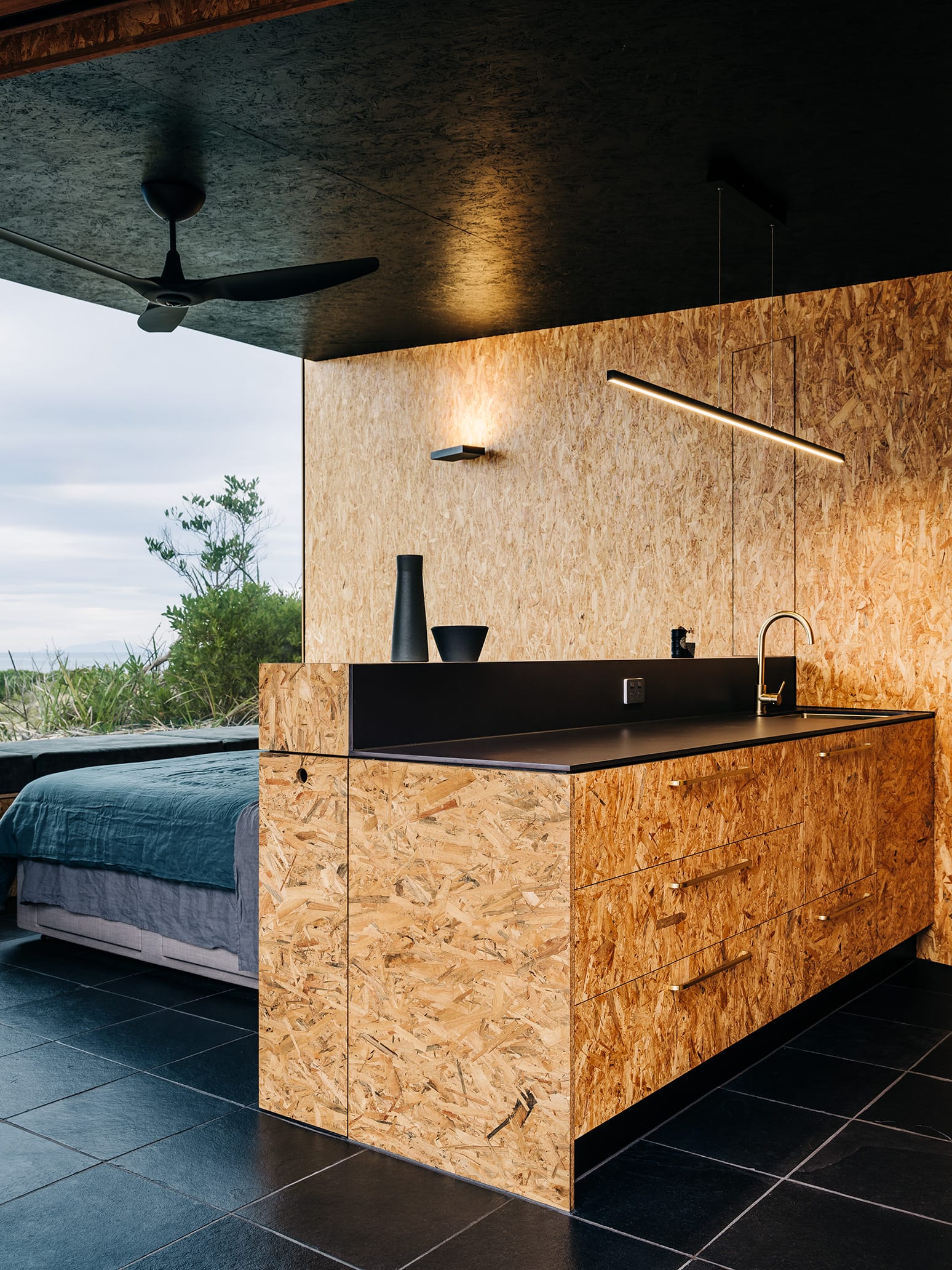 Studio Tasmania. Photography by Adam Gibson. Kitchen counters made from plywood, with black countertops, black tiled floors and plywood walls.