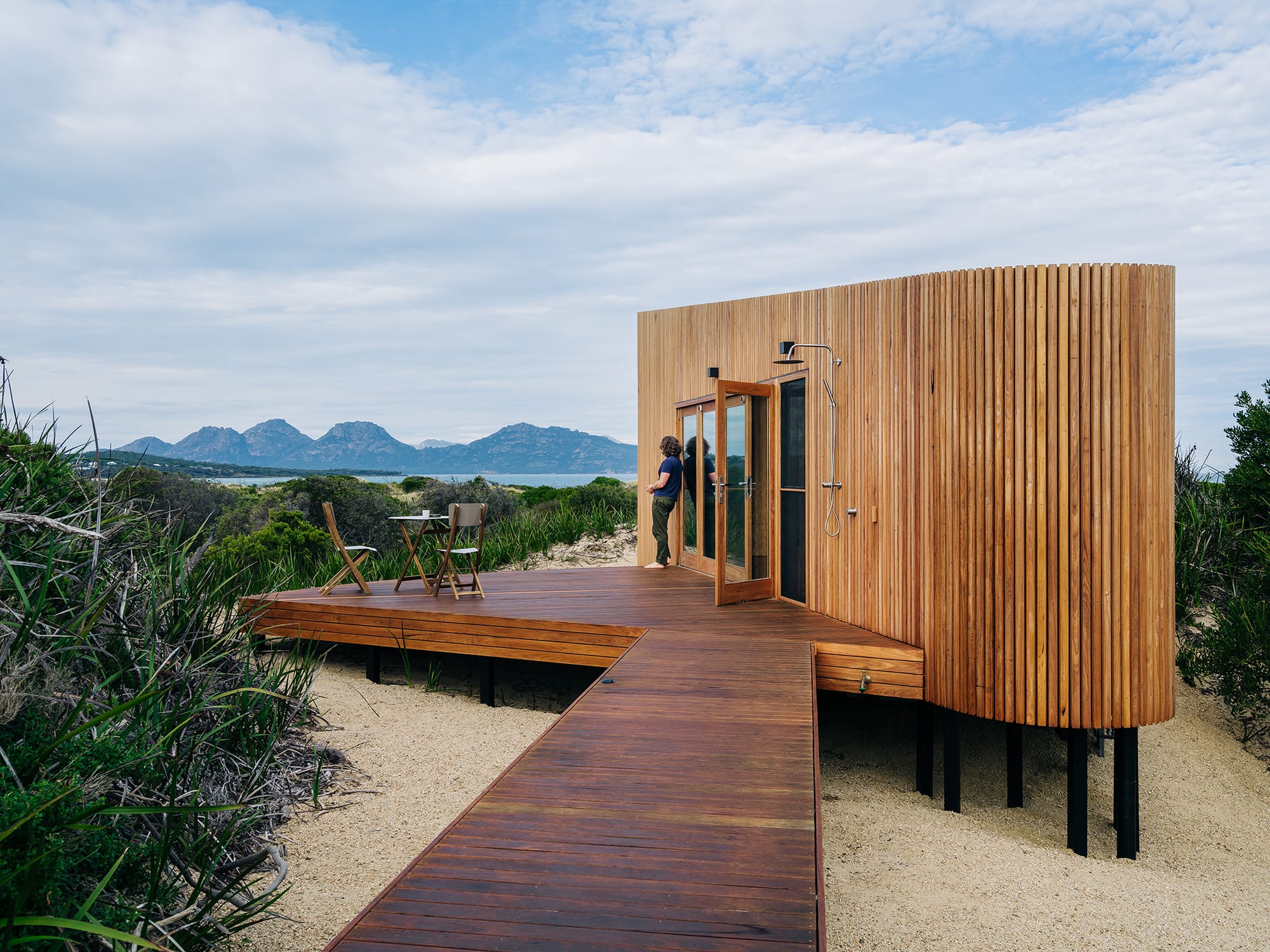 Studio Tasmania. Photography by Adam Gibson. Timber beach hut with deck and boardwalk across sand.