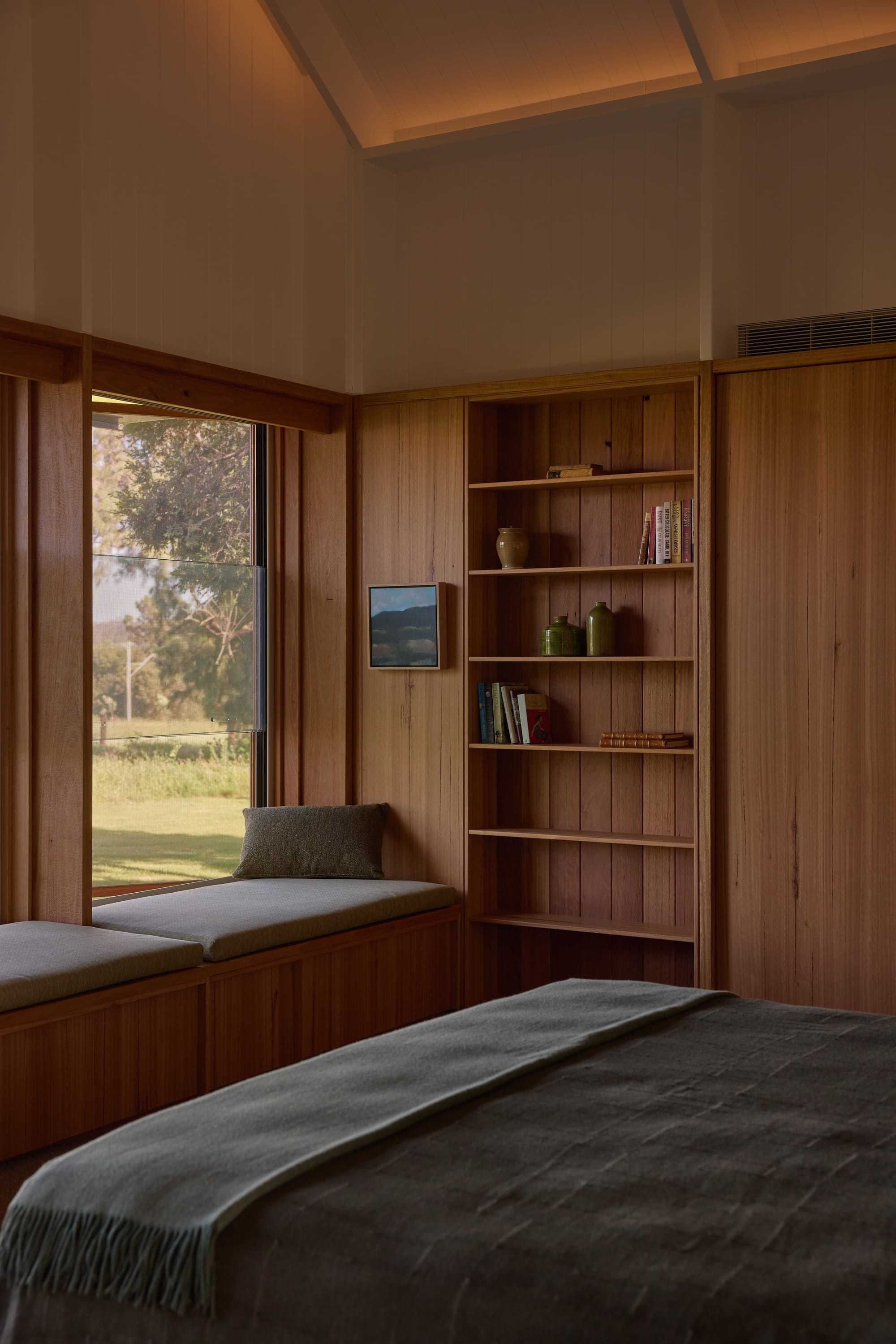 Binnum Homestead by Alexandra Buchanan Architecture. Photography by Cieran Murphy. Bedroom with built-in window seating with timber bench and green cushion, timber clad walls and timber integrated bookshelf.