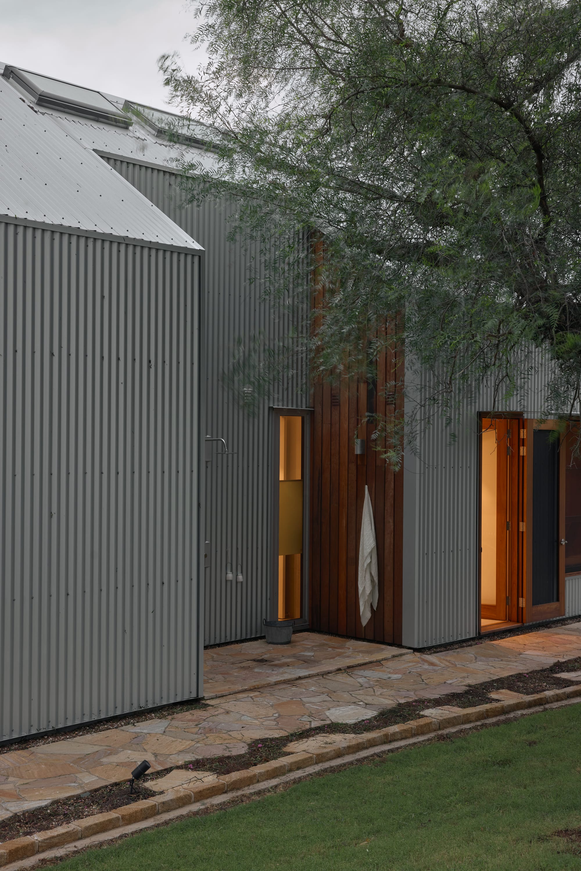 Binnum Homestead by Alexandra Buchanan Architecture. Photography by Cieran Murphy. Facade of home finished with corrugated iron cladding, with timber clad doors and sandstone paver pathway.