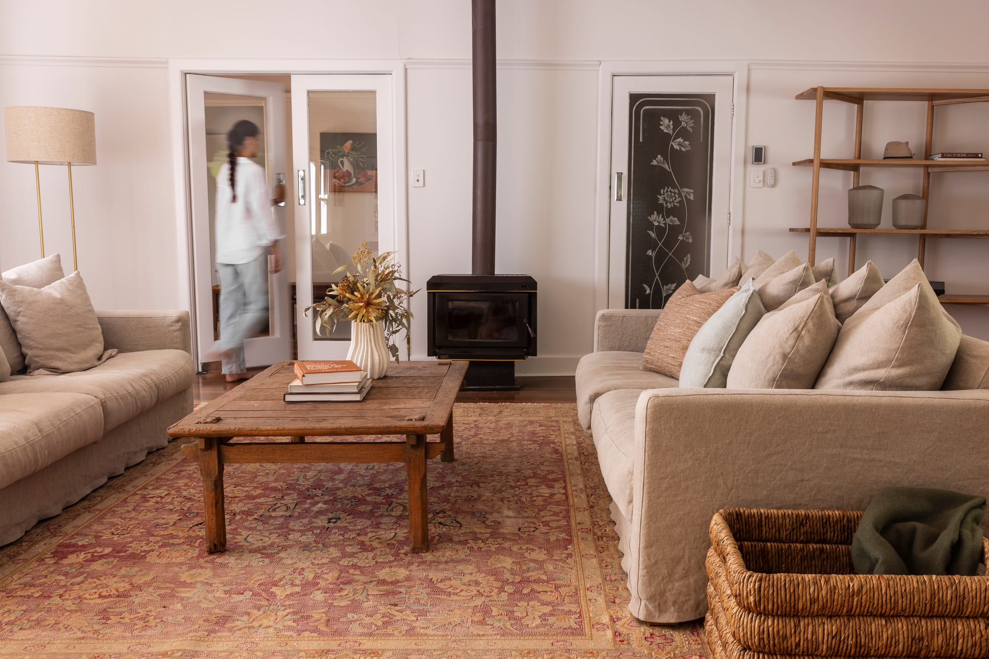 The Cottage by Bel.Bon Design. Photography by Sana Brotherson. Living space with faded Persian floor rug, two light beige linen sofas, reclaimed timber coffee table and black fireplace.