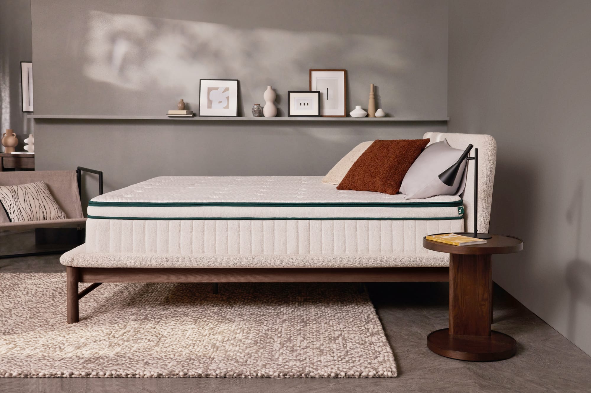 Luxe Mattress by Koala. Bed with white exposed mattress in room with grey walls, grey floor tiles, white and beige floor rug and timber side table.