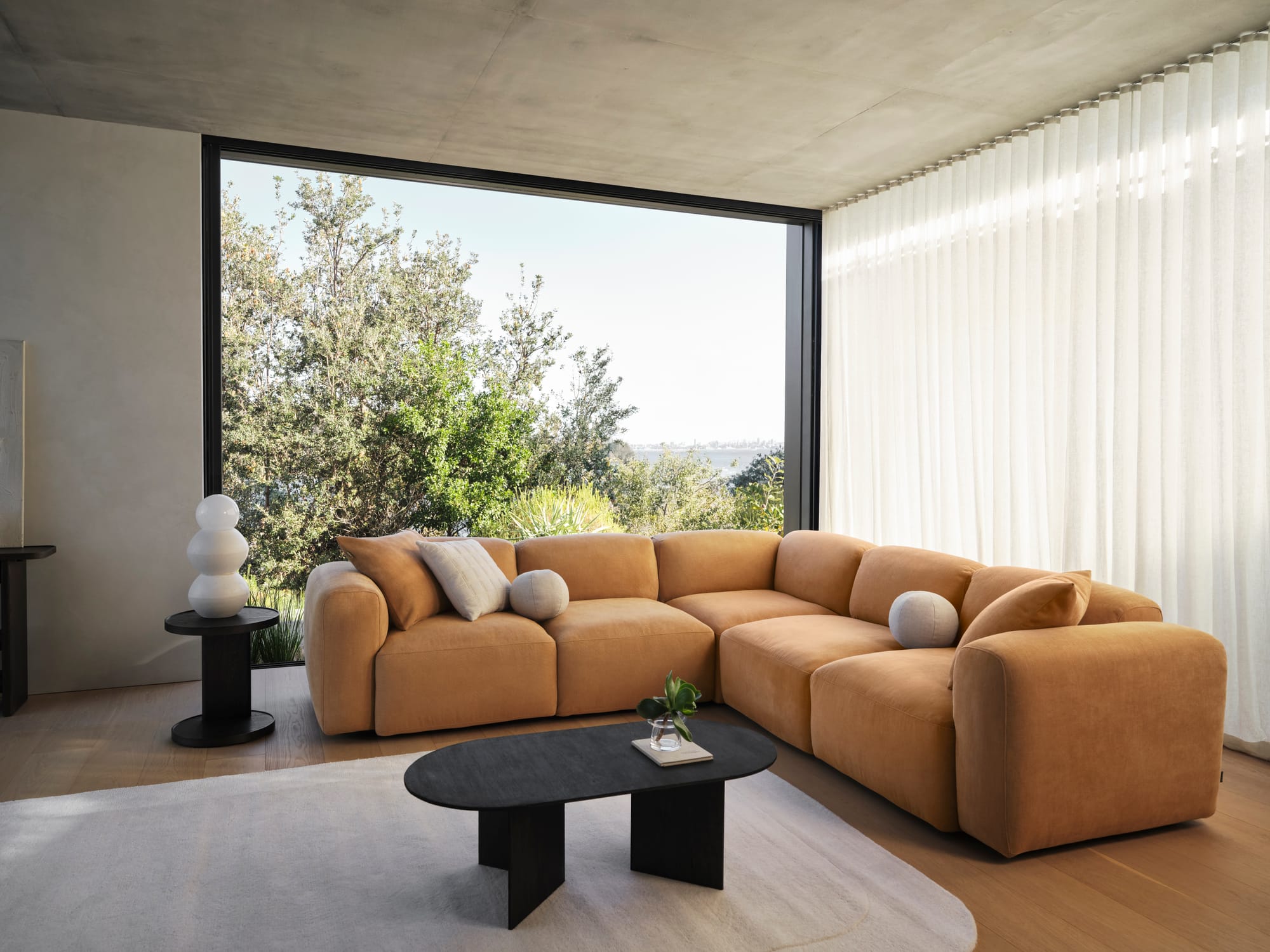 Torquay Sofa in Bronzed Aussie by Koala. Mustard yellow couch in room with timber floors, black coffee table and full height windows overlooking bushland.