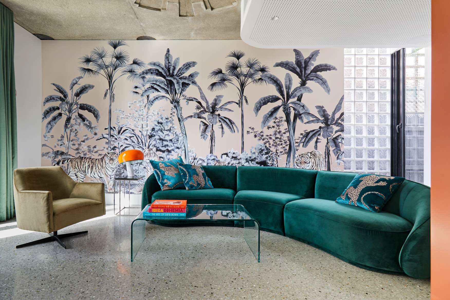 Park St by SGKS ARCH. Photography by Tania Lee. Living space with emerald curved couch, concrete floors, and palm-tree patterned wallpaper.