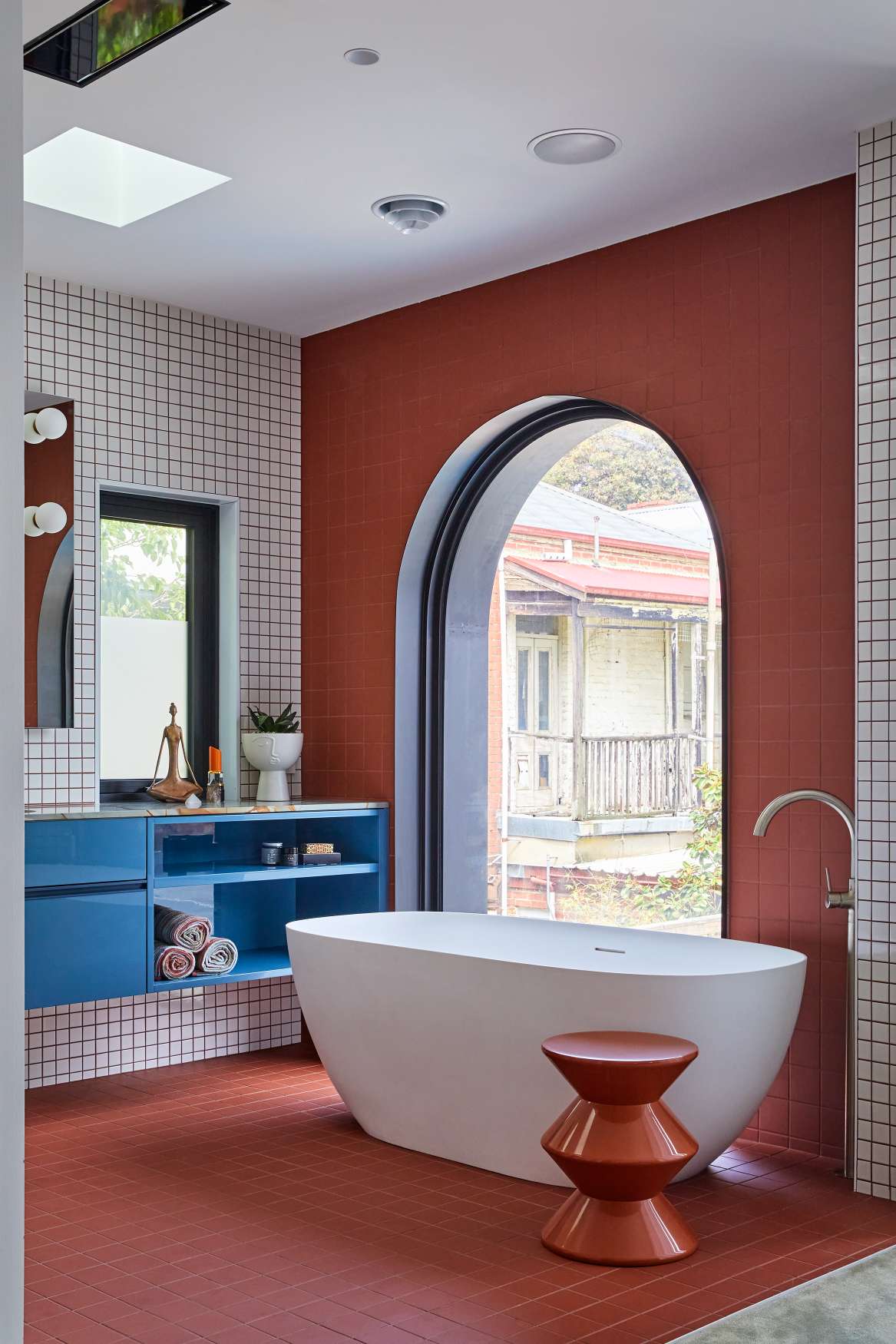 Park St by SGKS ARCH. Photography by Tania Lee. Bathroom with terracotta floor tiles, white tub and blue open-faced storage and vanity.