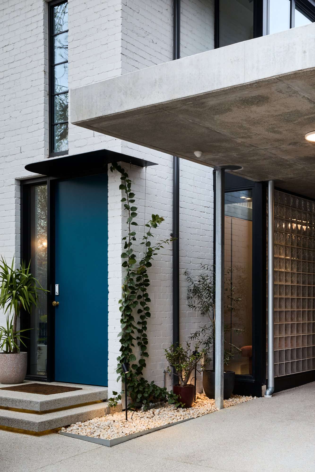 Park St by SGKS ARCH. Photography by Tania Lee. Brick building painted white with teal front door, concrete pavers and glass brick wall.